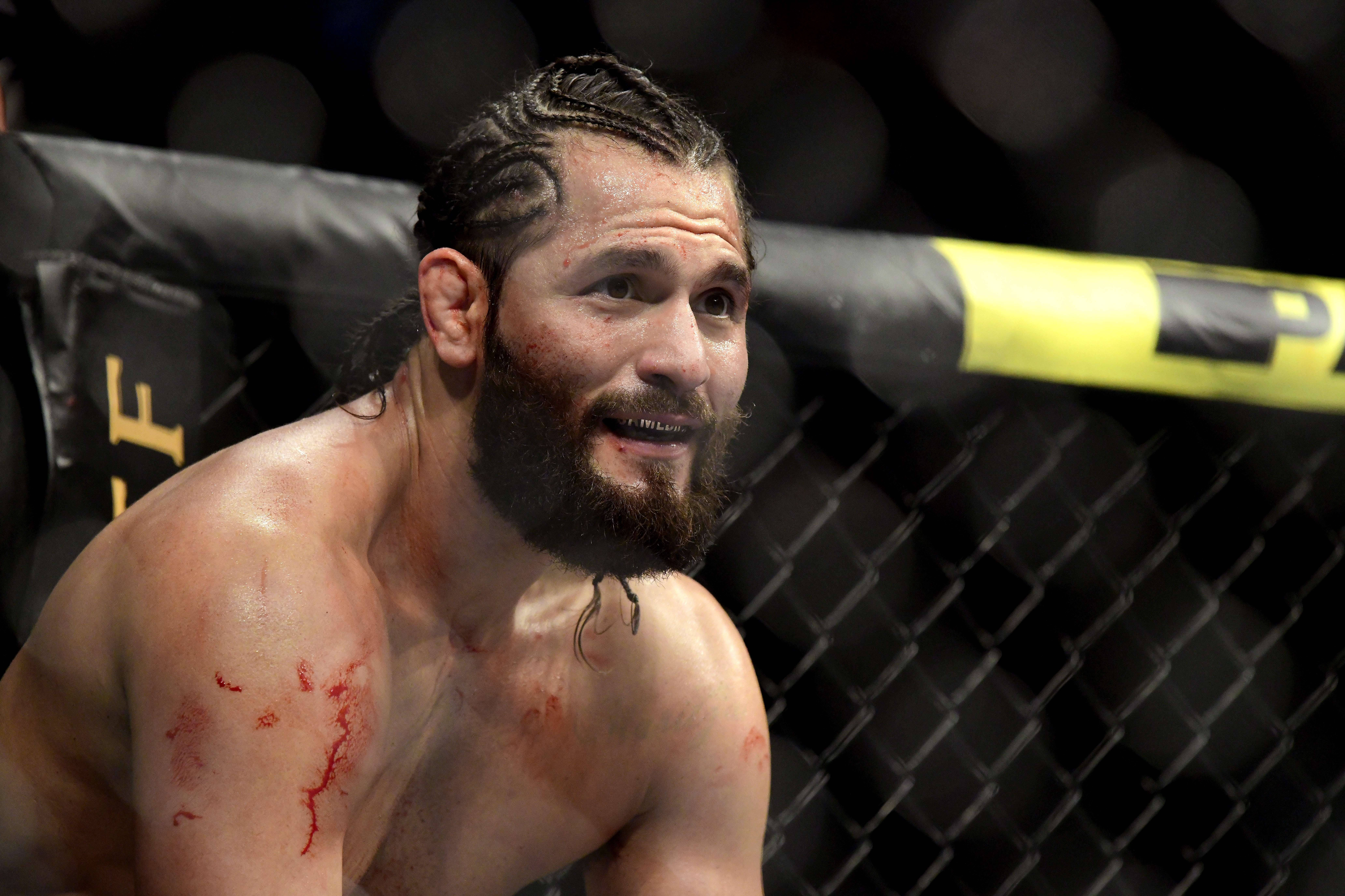 血跡斑斑的Jorge Masvidal 壁紙 — 一名滿身鮮血、辮子頭髮和鬍鬚的MMA拳手在黃色邊框的籠內顯得神情專注。