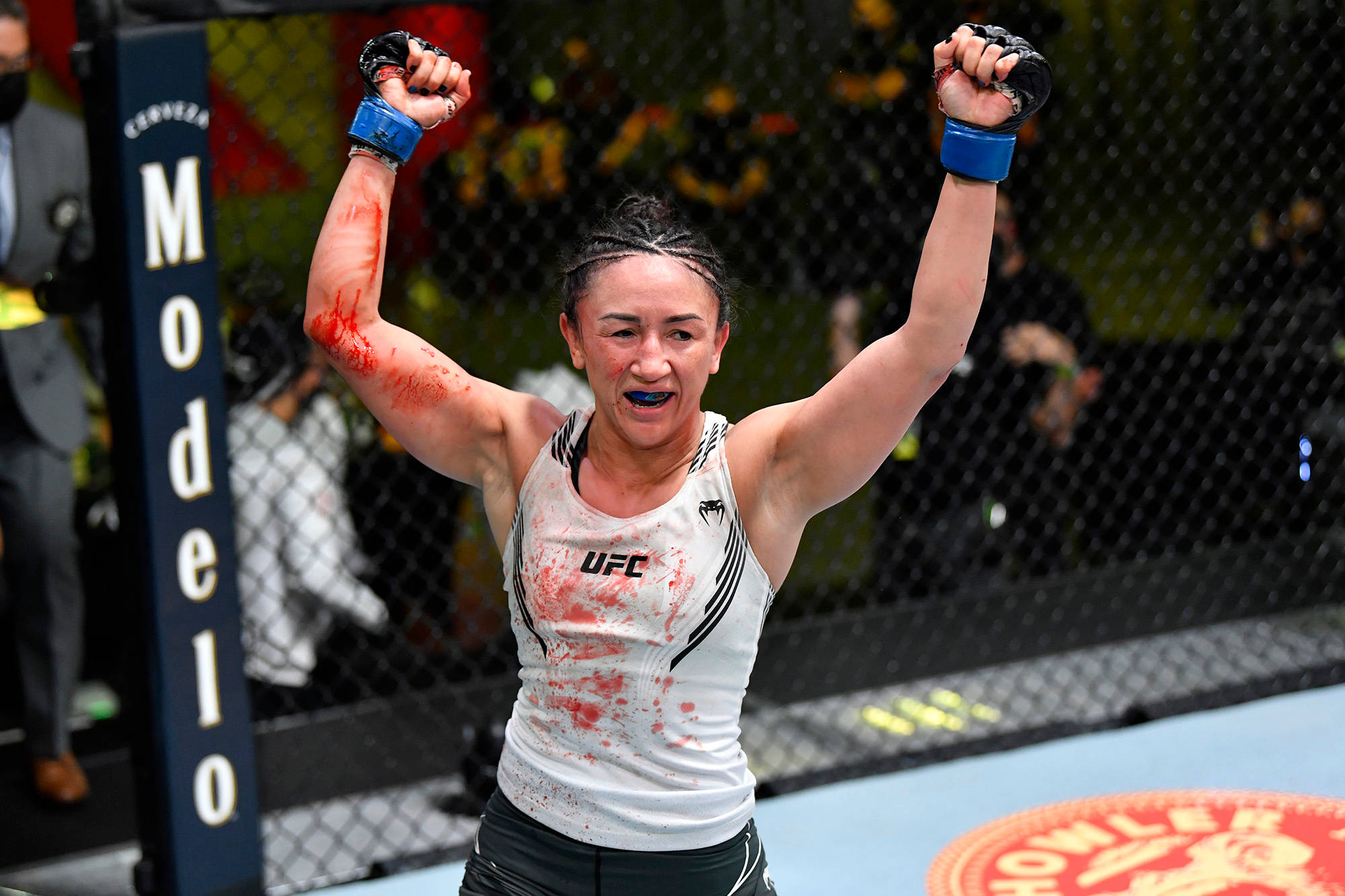 血跡斑斑的卡菈·艾斯帕薩 壁紙 — 一位勝利的女性MMA拳手在UFC賽事中，於血跡斑斑的八角籠內高舉拳頭慶祝勝利。