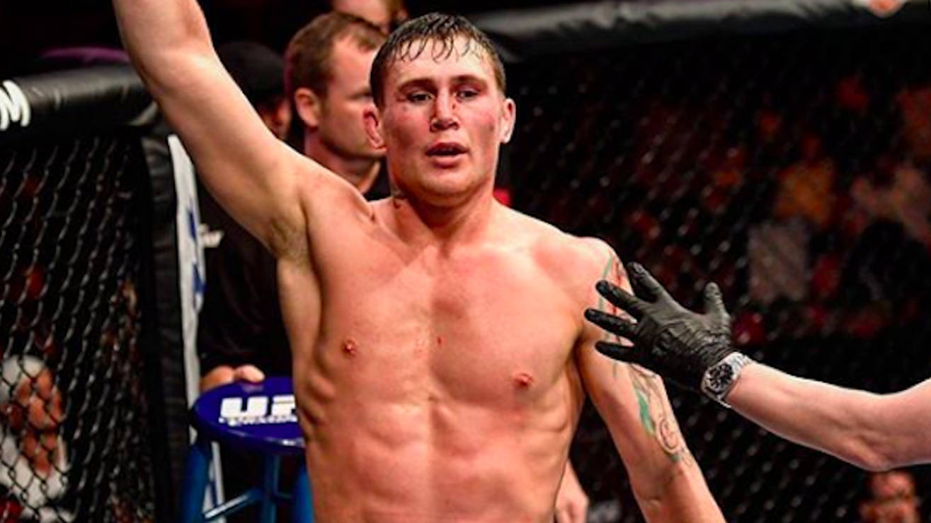 血跡斑斑的達倫·提爾勝利舉臂 壁紙 — 一位勝利的綜合格鬥選手在UFC八角籠內高舉手臂慶祝勝利，裁判的手放在他的肩膀上。