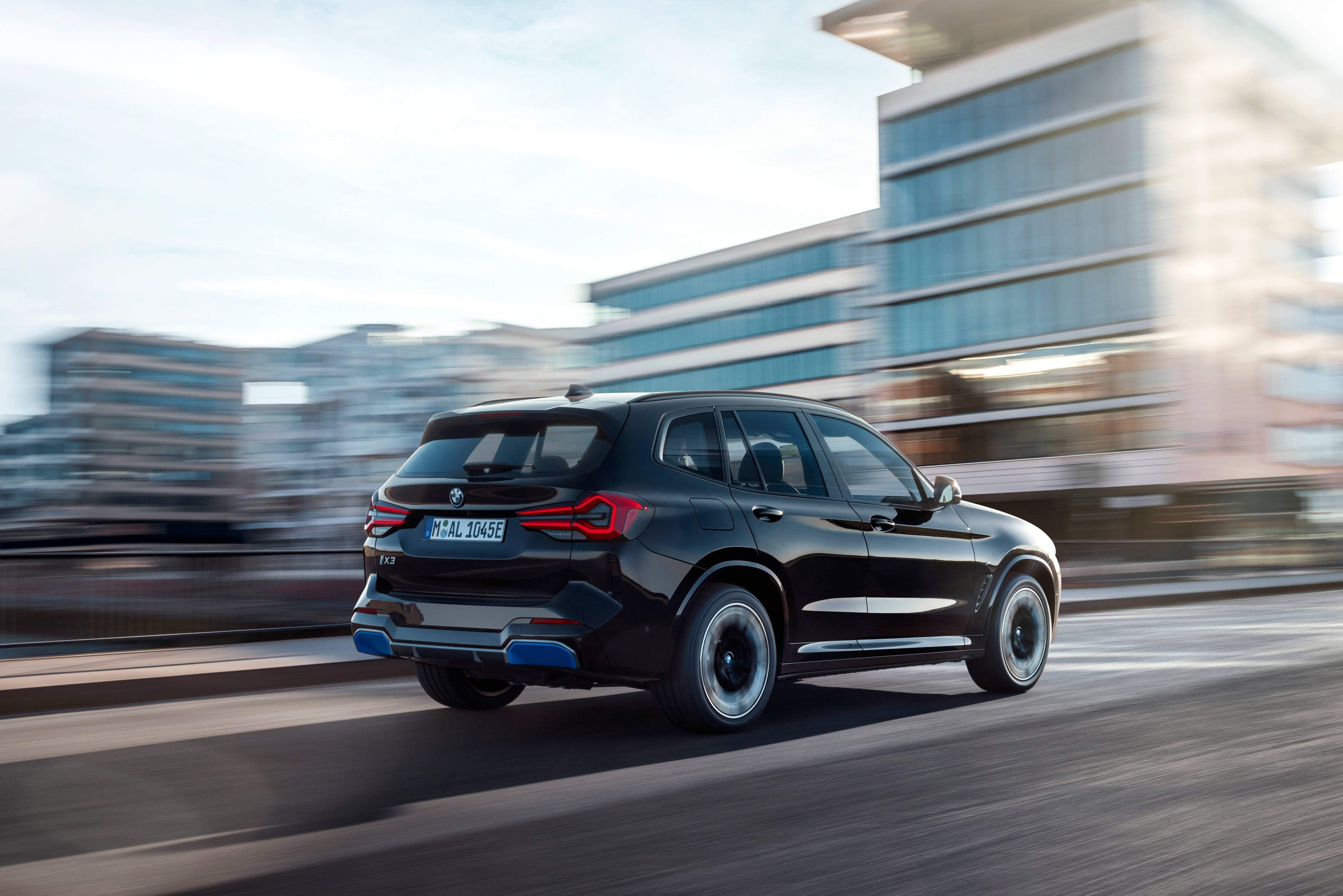 行駛中的黑色BMW IX3 M Sport 壁紙 — 一輛時尚的黑色BMW SUV在現代城市景觀中疾馳，背景帶有動態模糊效果。