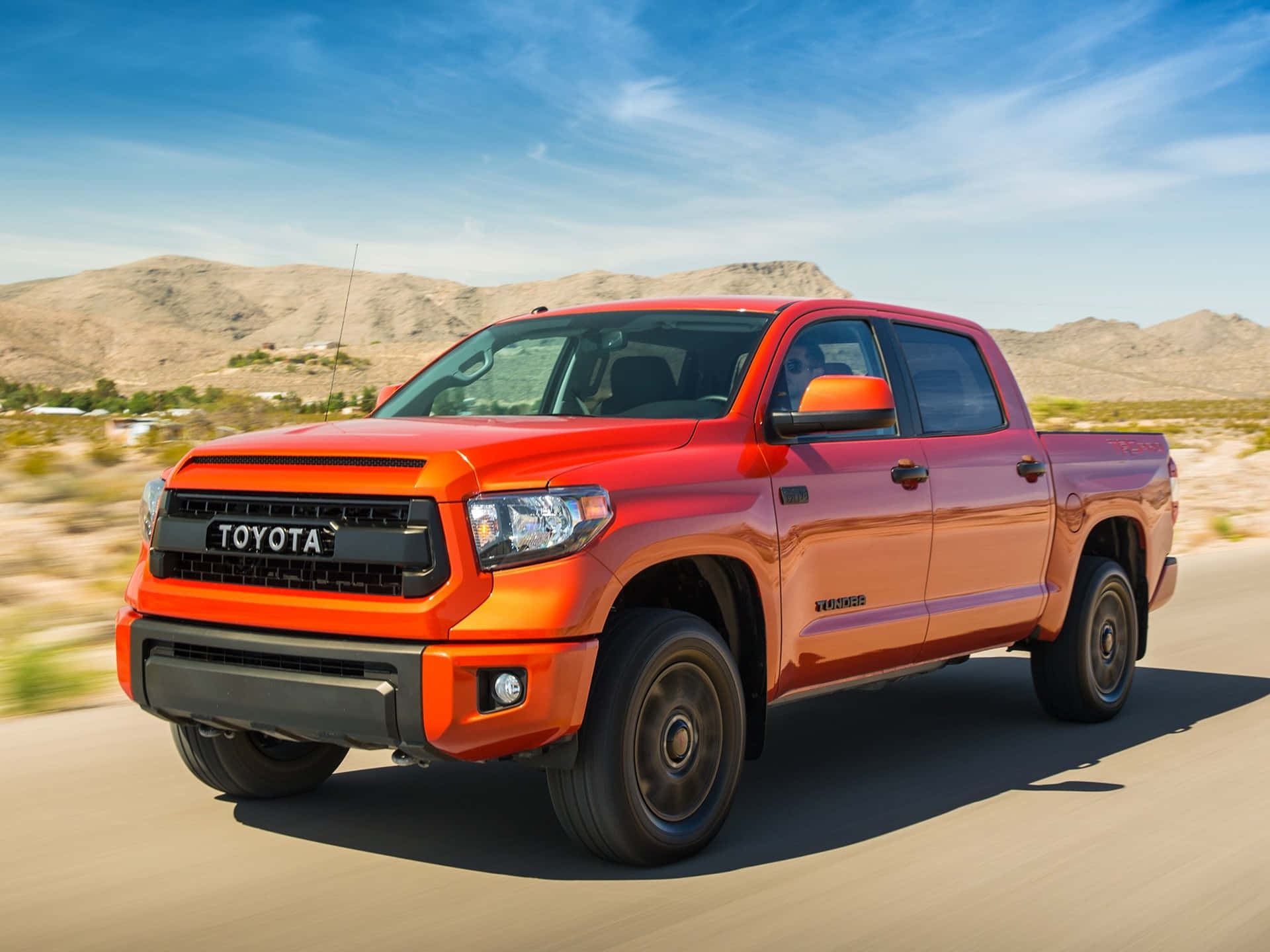 橙色豐田Tundra pickup truck在沙漠公路上快速行駛，背景有山脈。