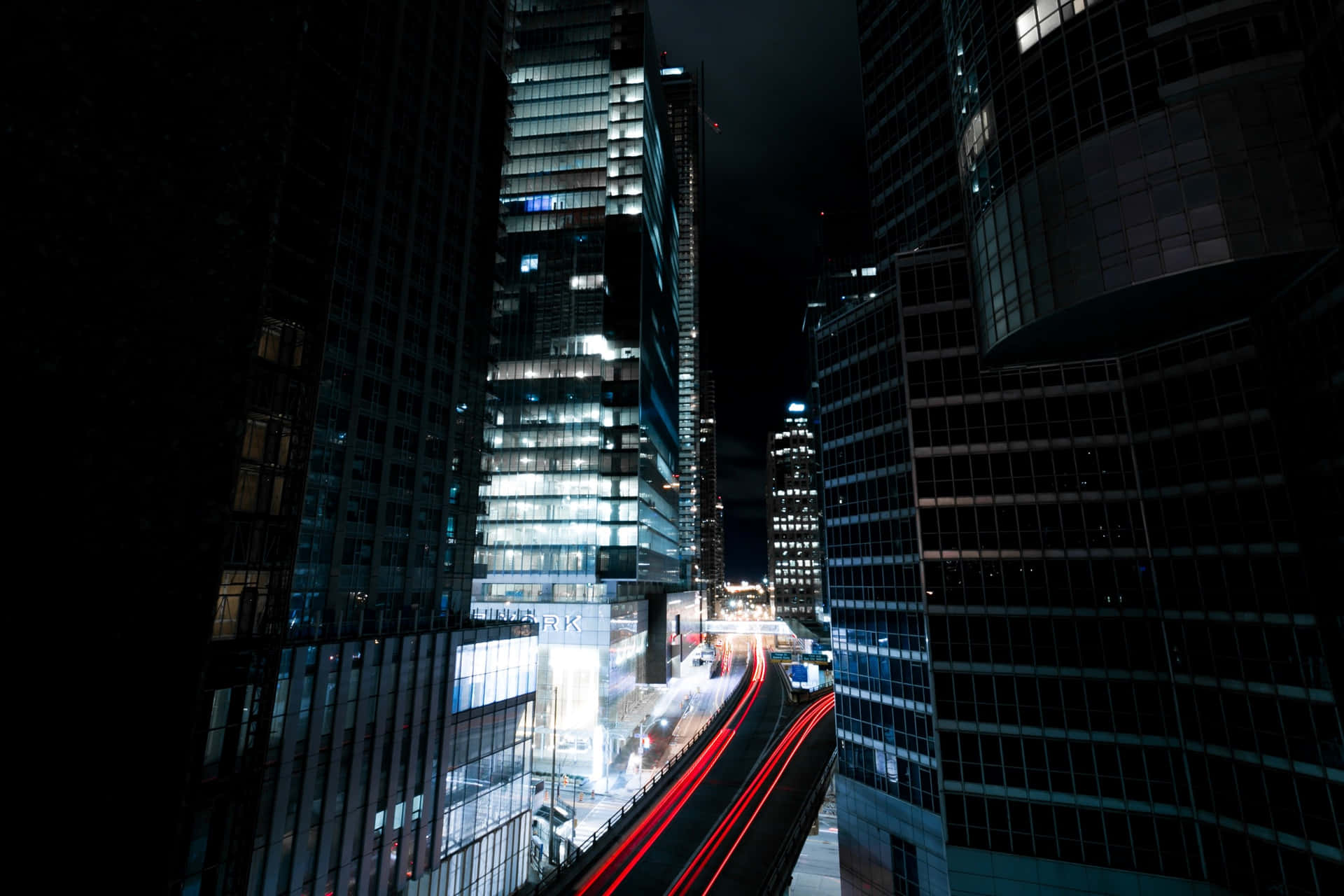 夜晚高聳的城市建築，帶有移動汽車的紅色光條。