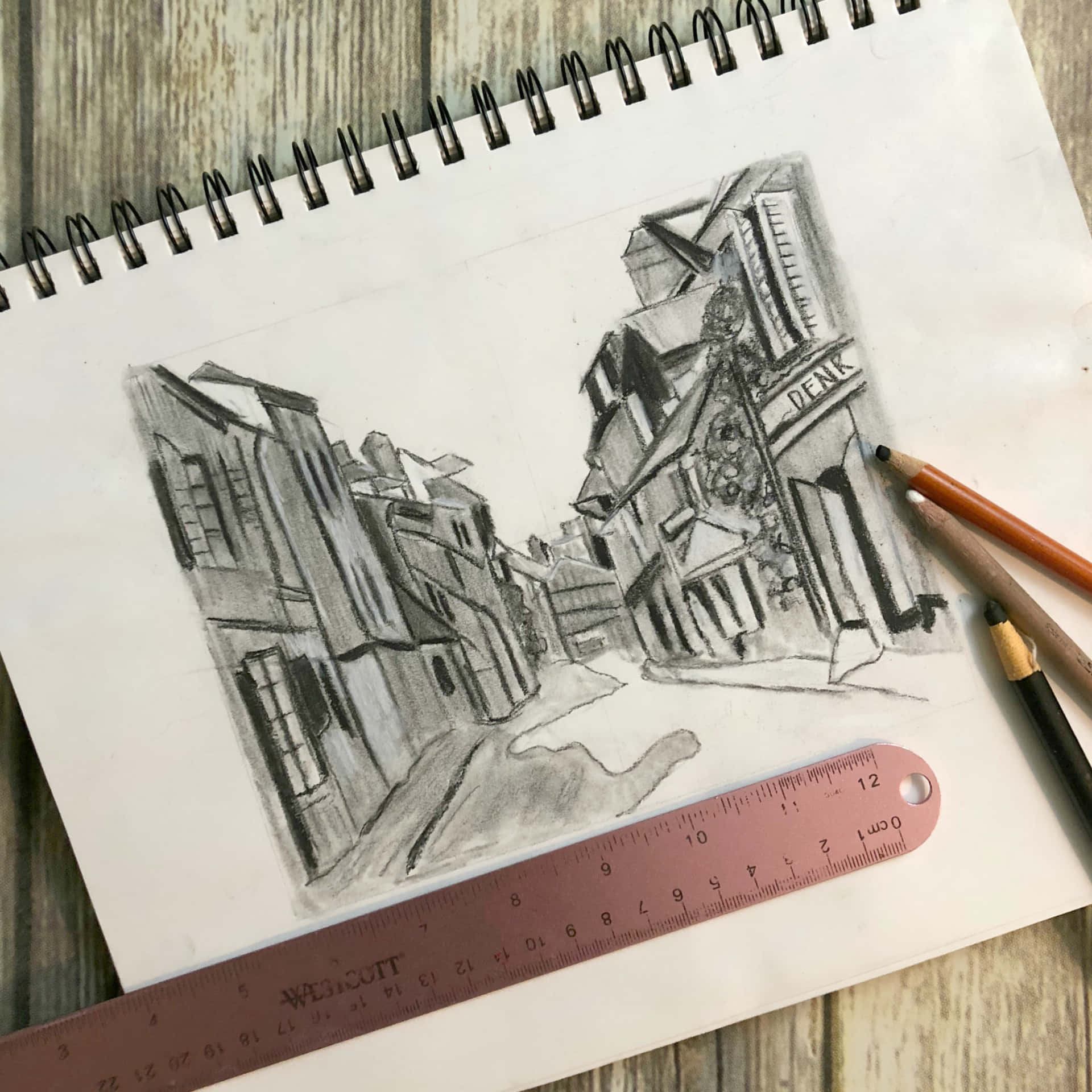 一幅鉛筆畫，描繪了帶有建築物和標誌的街景，周圍是木頭上的藝術工具。