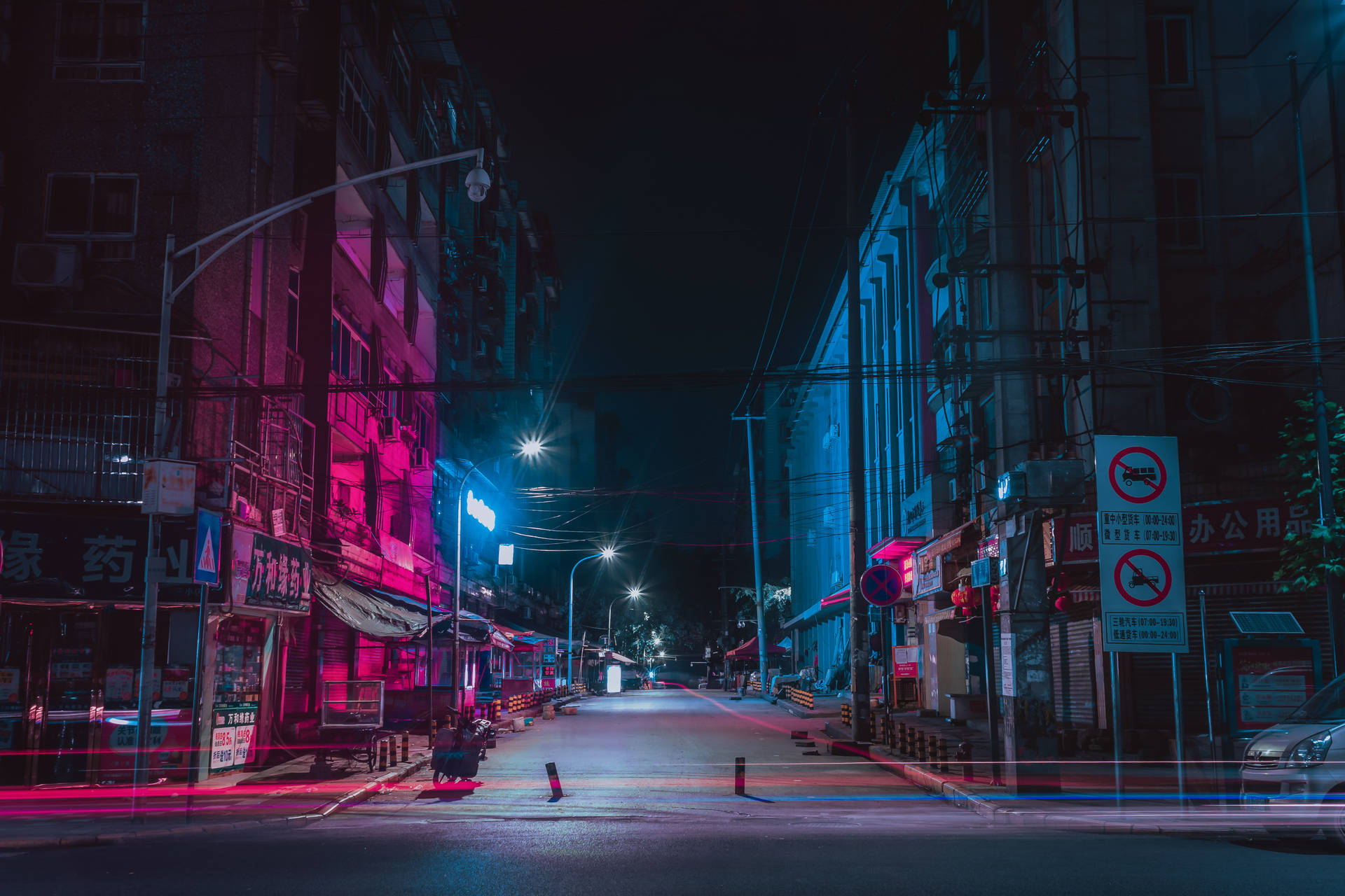 夜晚空無一人的霓虹燈都市街道，濕漉漉的路面上有粉紅色和藍色的倒影。