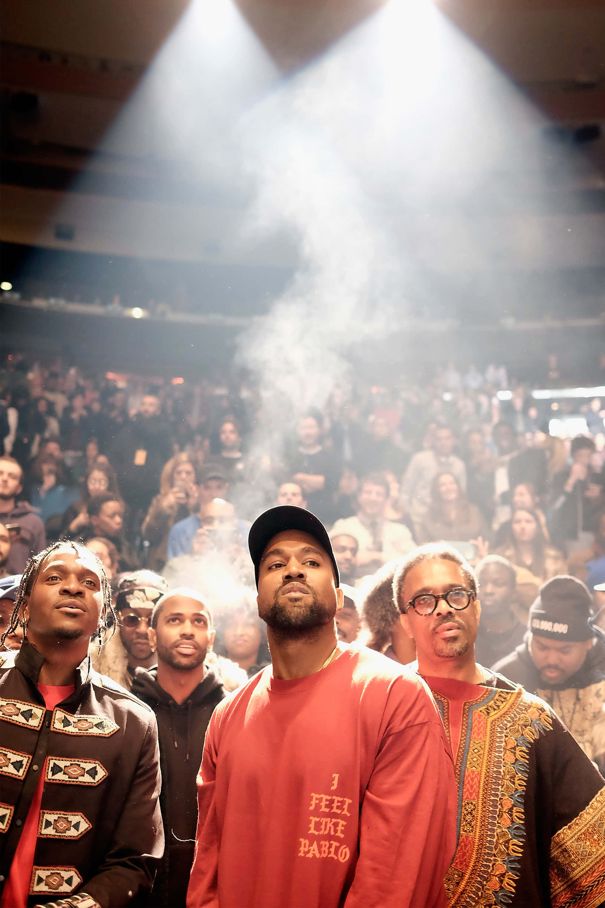 街頭塗鴉藝術呈現《The Life Of Pablo》 壁紙 — 三位身穿圖案服裝的男子在明亮的聚光燈下站在舞台中央，煙霧繚繞，面前是擠滿的音樂會人群。