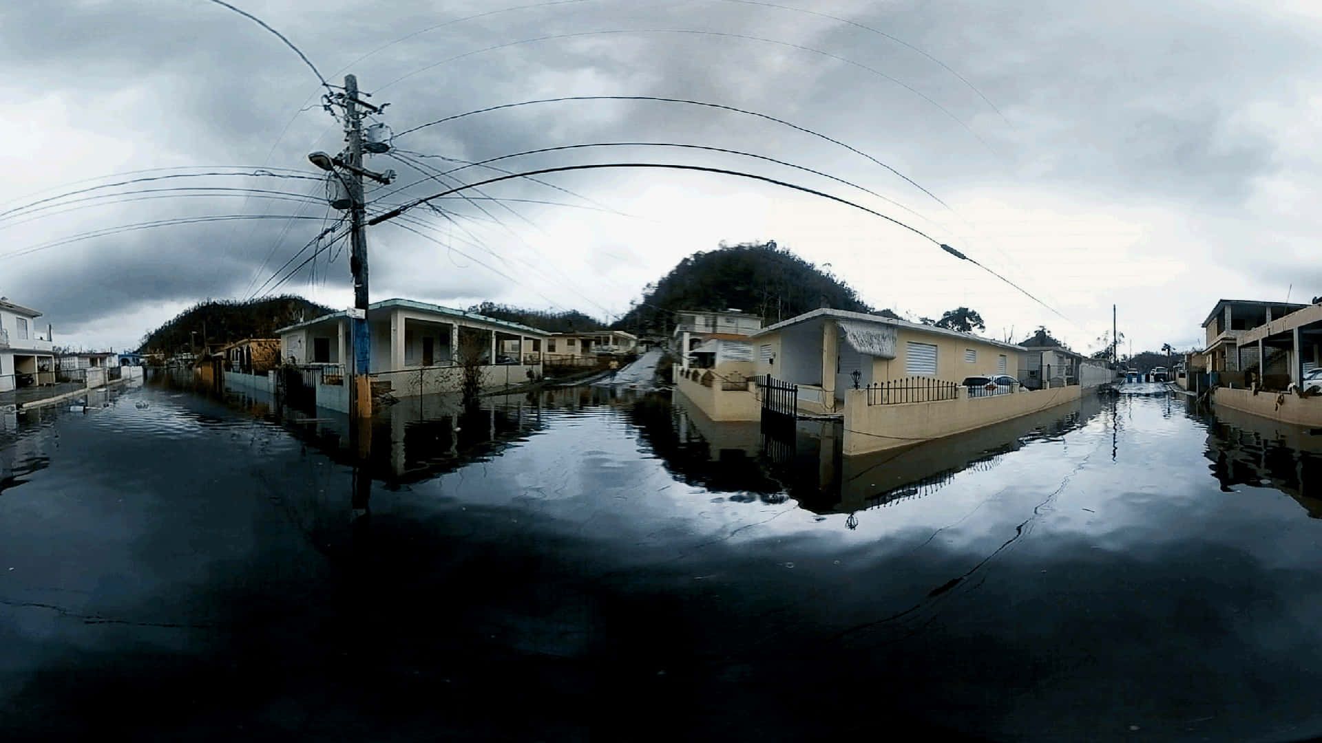 街頭洪災360度照片 壁紙 — 在沉重的灰色天空下，被淹沒的街道上有被水淹沒的房屋和電線。