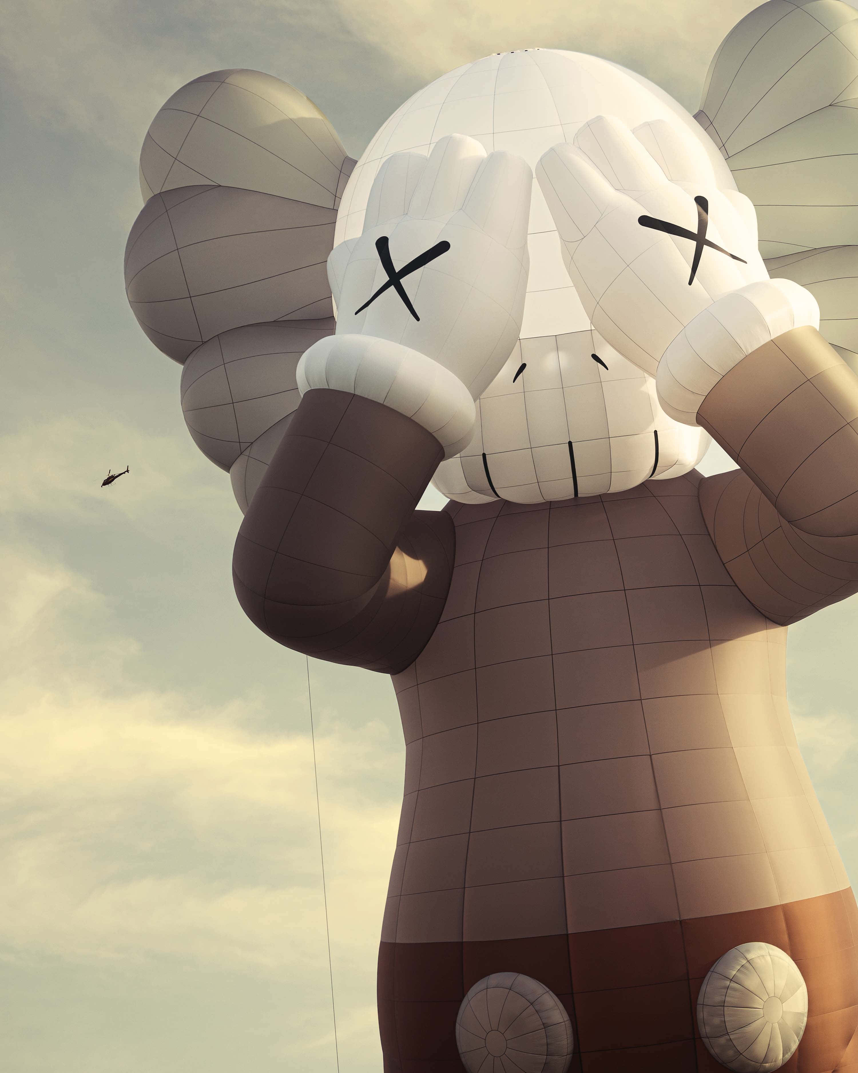 街頭藝術家 Kaws 的經典作品 壁紙 — 一個巨大的白色氣球雕塑，描繪KAWS角色，擁有X形眼睛並用手遮住臉龐，背景為多雲的天空。