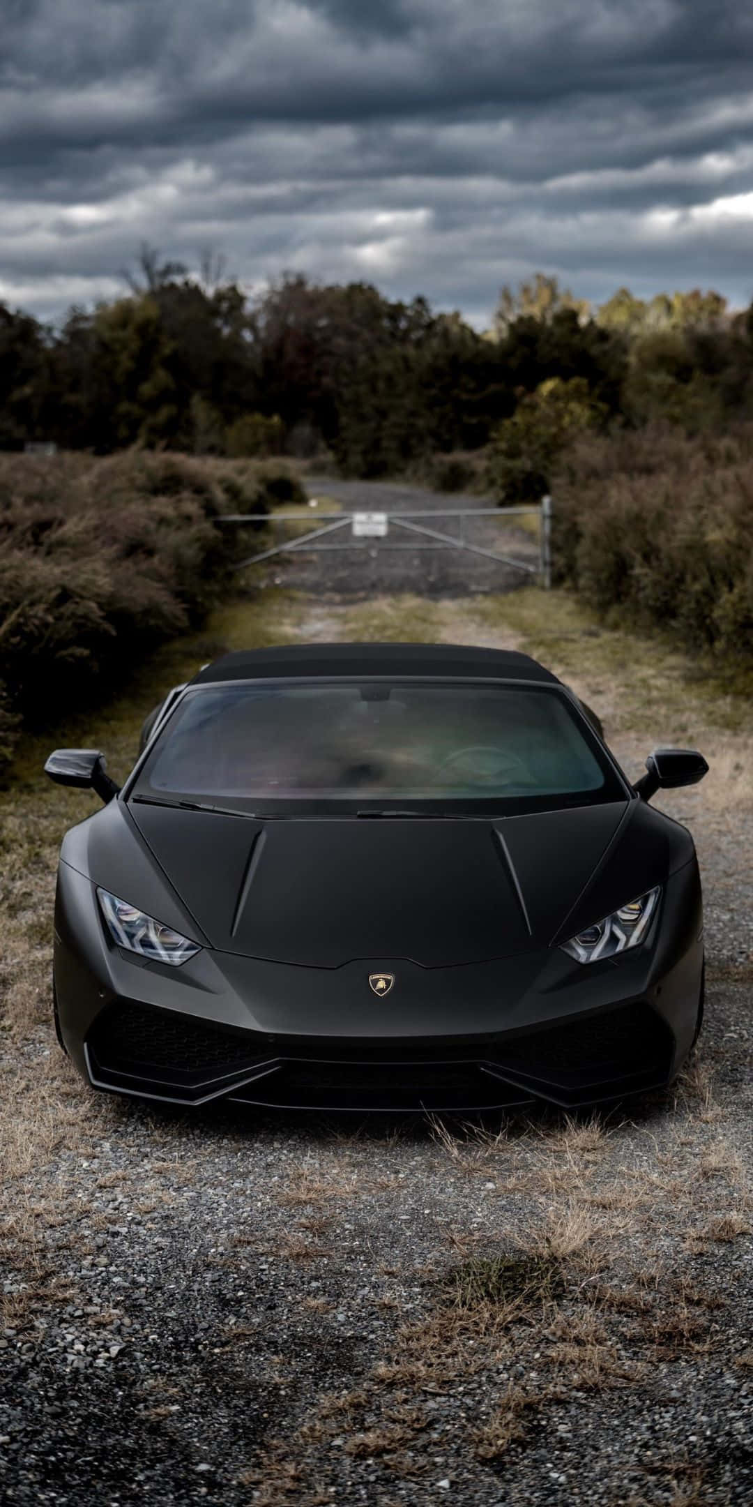 街頭風格的 Lamborghini，以 Pixel 3 獨特設計塗裝 壁紙 — 一輛啞光黑色的林寶堅尼 Huracán 停泊在碎石路上，背景是暴風雨的天空和秋天的樹木。