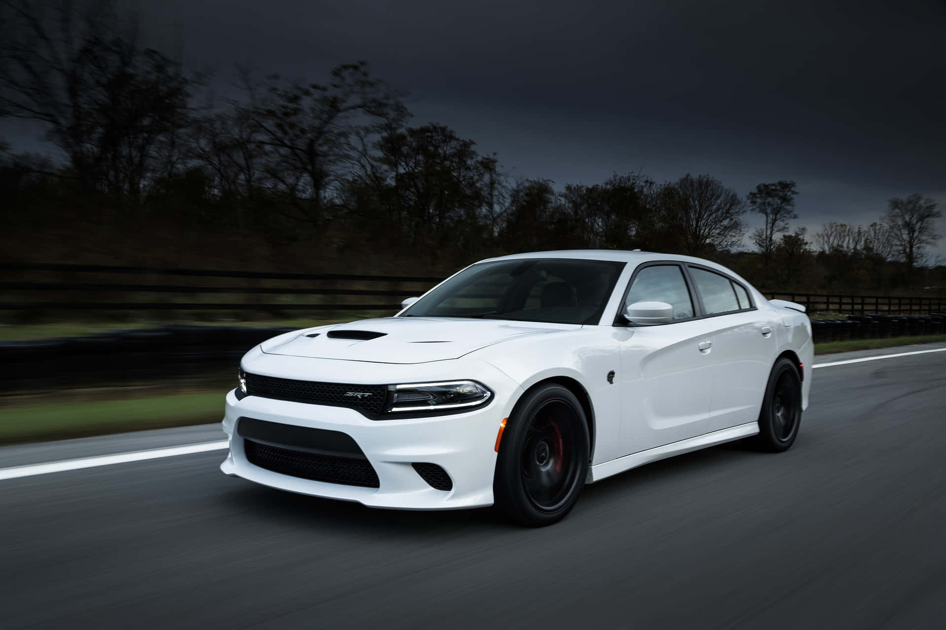 白色Dodge Charger RT在暴風雨的天空下在潮濕的道路上疾馳。