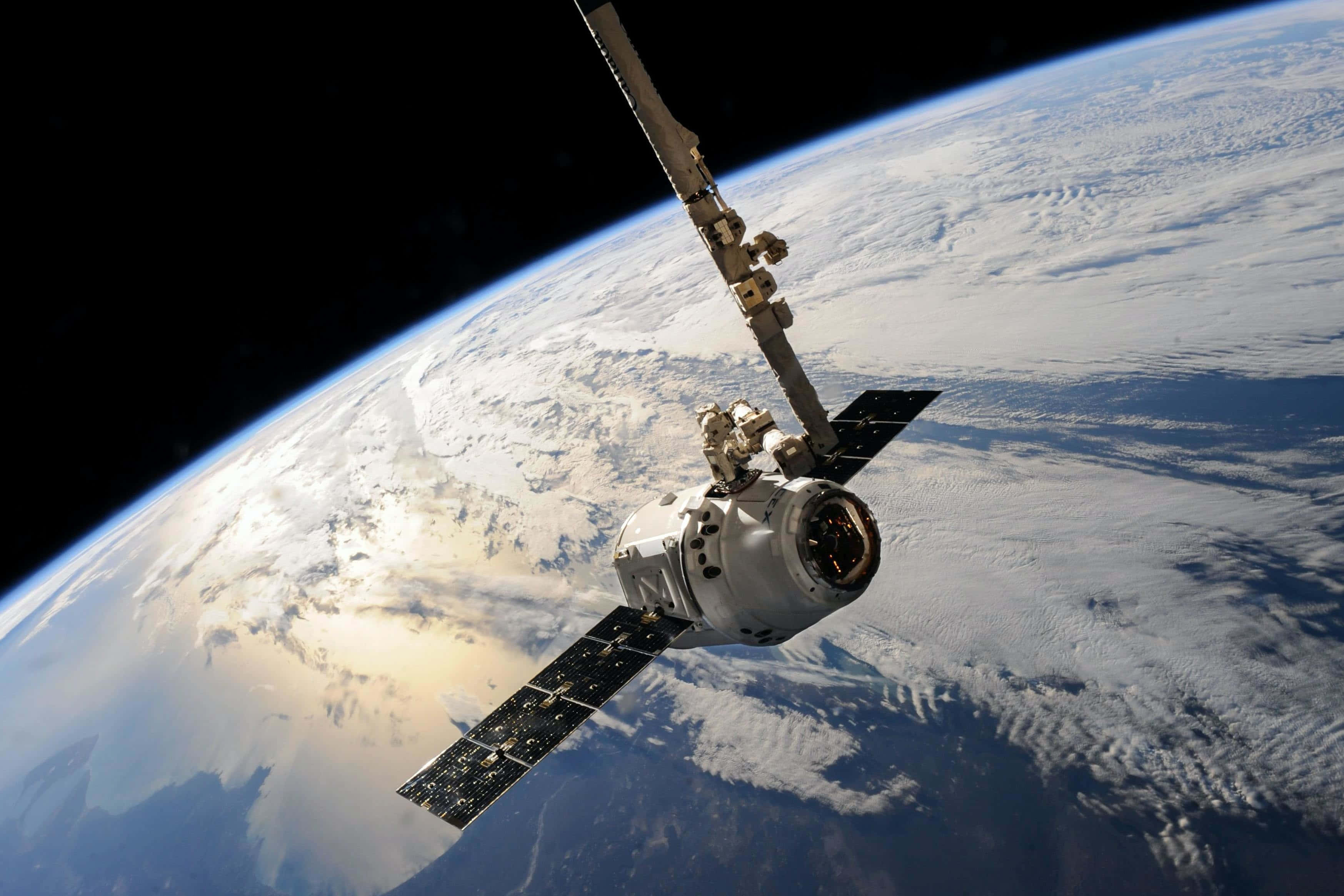 衛星環繞遙遠行星 壁紙 — 一艘帶有太陽能板的太空船繞地球軌道運行，顯示被雪覆蓋的大陸和海洋，背景是太空的漆黑。