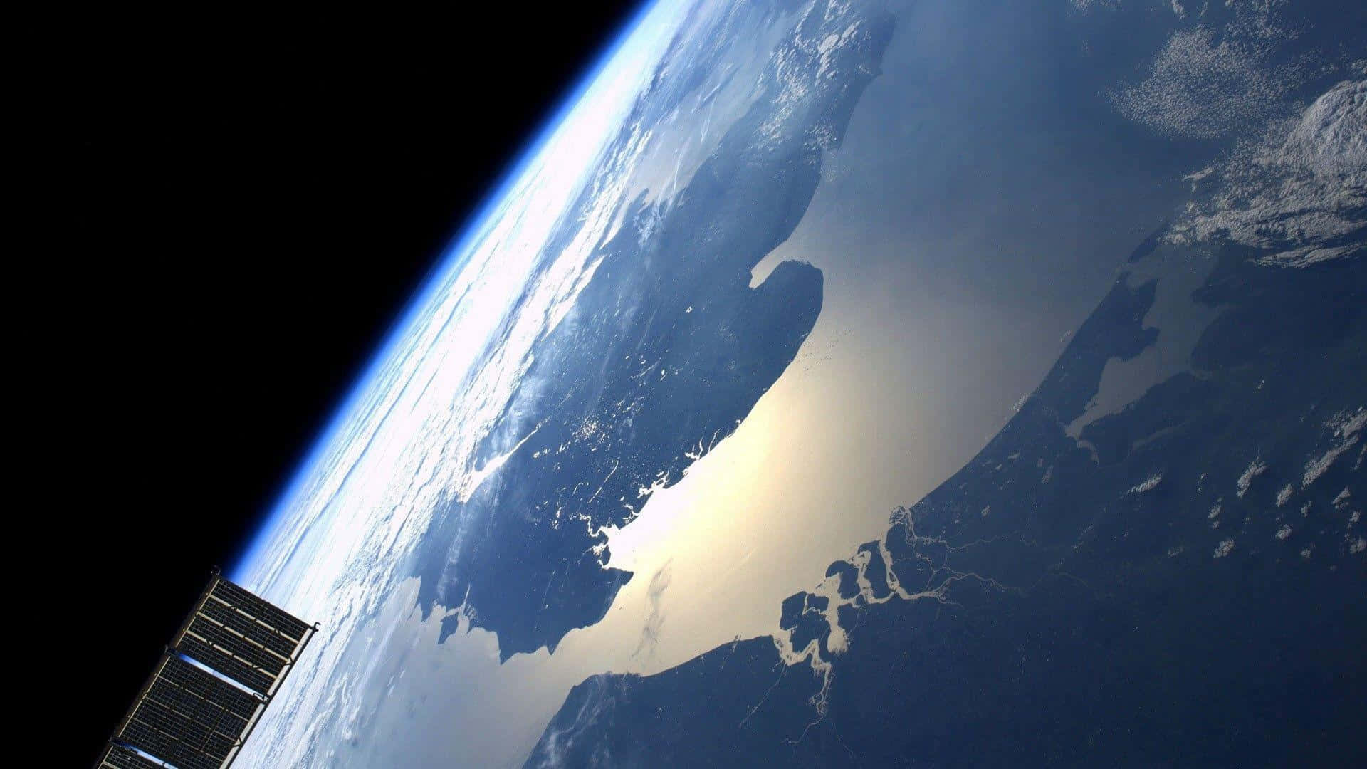 Satellite 桌布 壁紙 — 衛星的太陽能板延伸至虛空，旁邊是地球彎曲的地平線，在陸地和海洋上空閃耀著日出光芒。