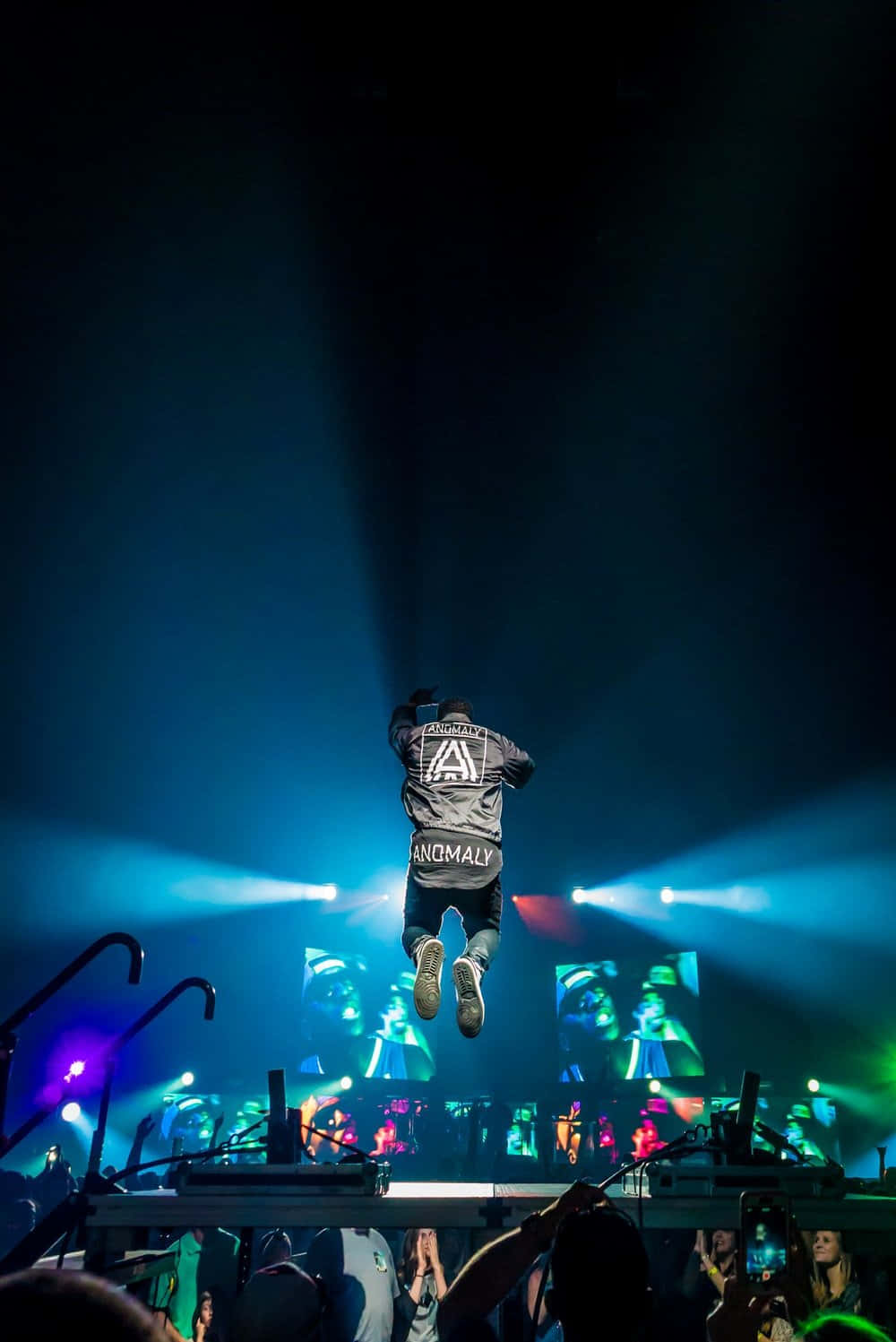Drake 桌布 壁紙 — 表演者在音樂會舞台上躍起，舞台沐浴在鮮豔的藍色和紫色聚光燈下，下方是投入的觀眾。