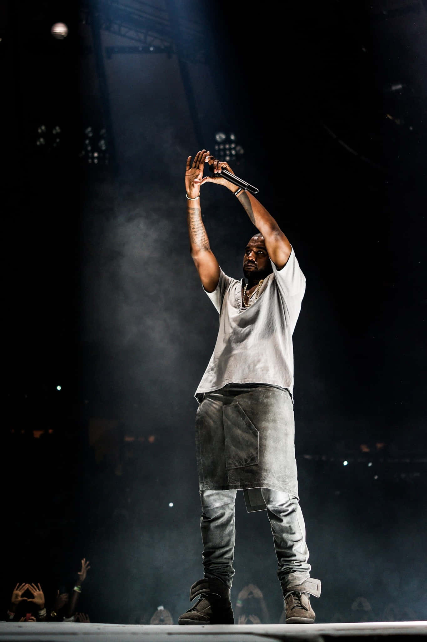 Kanye 桌布 壁紙 — 表演者站在舞台中央，高舉雙臂握著麥克風，在戲劇性的聚光燈下，煙霧在他周圍旋轉。