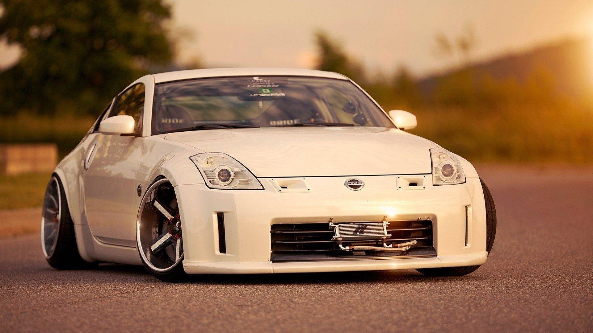 被 Nissan 350Z 吸引的靈感 壁紙 — 一輛純白色的日產350Z跑車在金色夕陽下，於一條寧靜的道路上閃閃發光，背景是模糊的綠意。