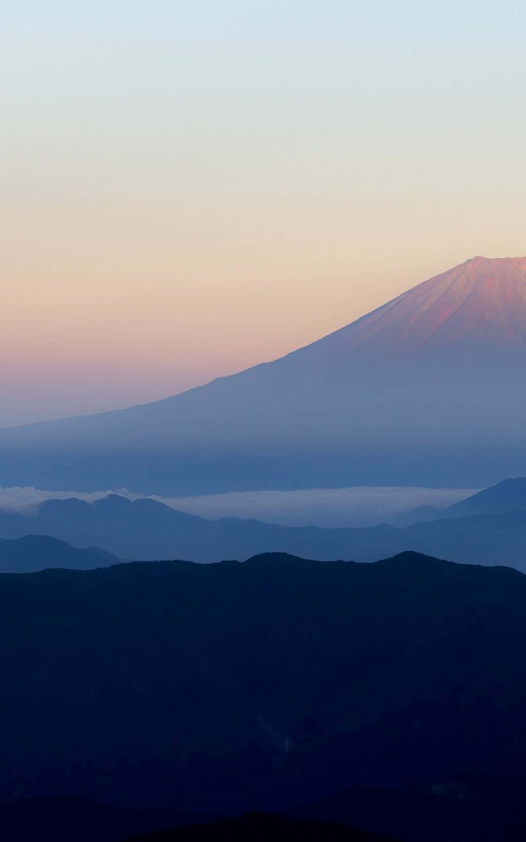 黎明時分的富士山，層疊山巒輪廓上空有粉紅色和藍色的天空。