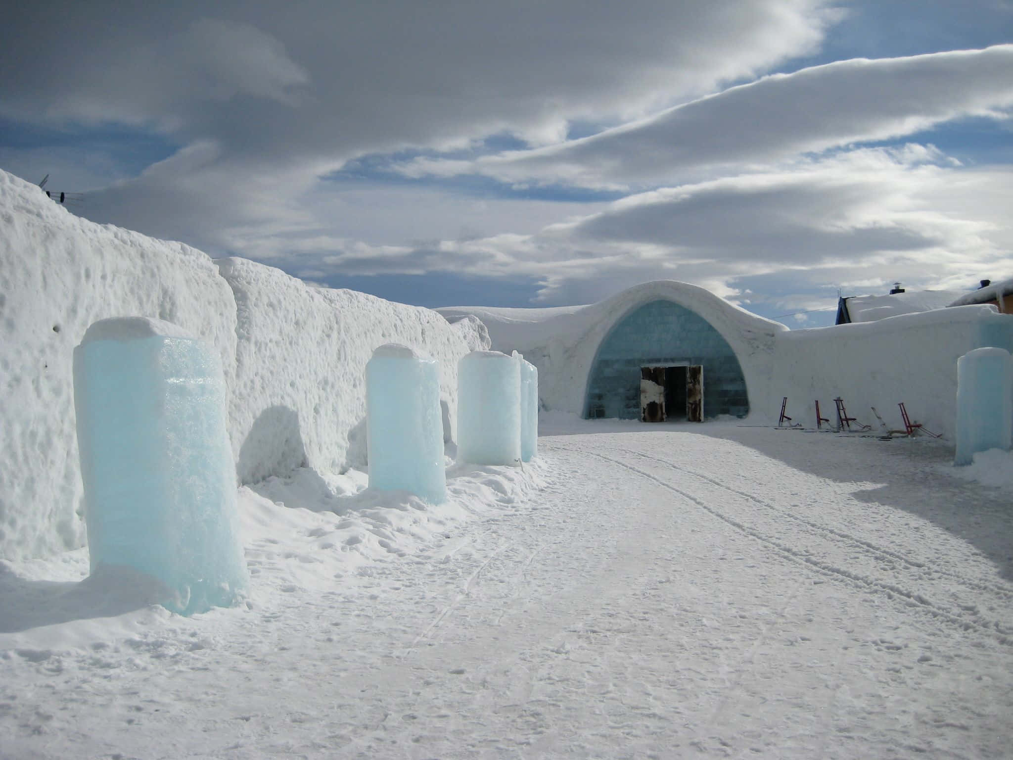 Ice Hotel 桌布 壁紙 — 被雪覆蓋的冰酒店，擁有半透明的藍色冰柱和拱形入口，天空多雲。