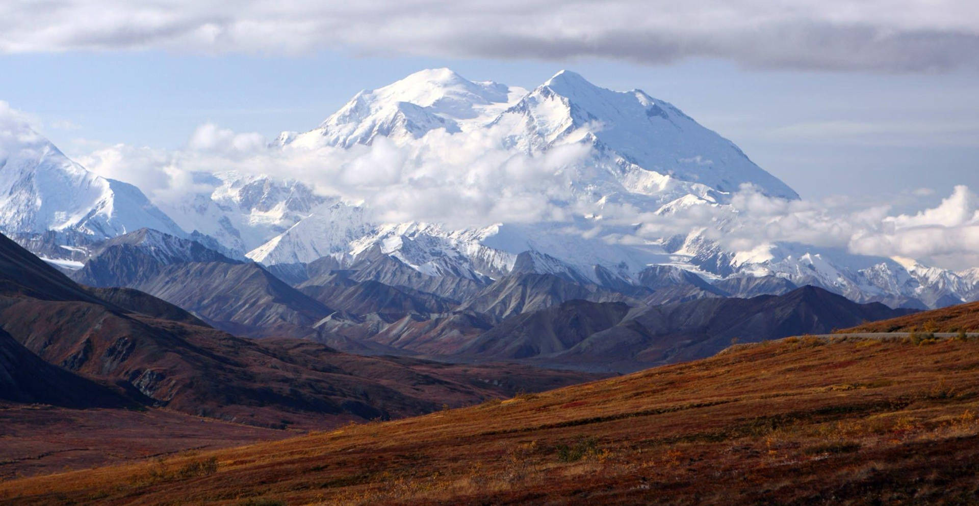 在多雲的天空下，雪山頂峰聳立在秋日山丘之上。