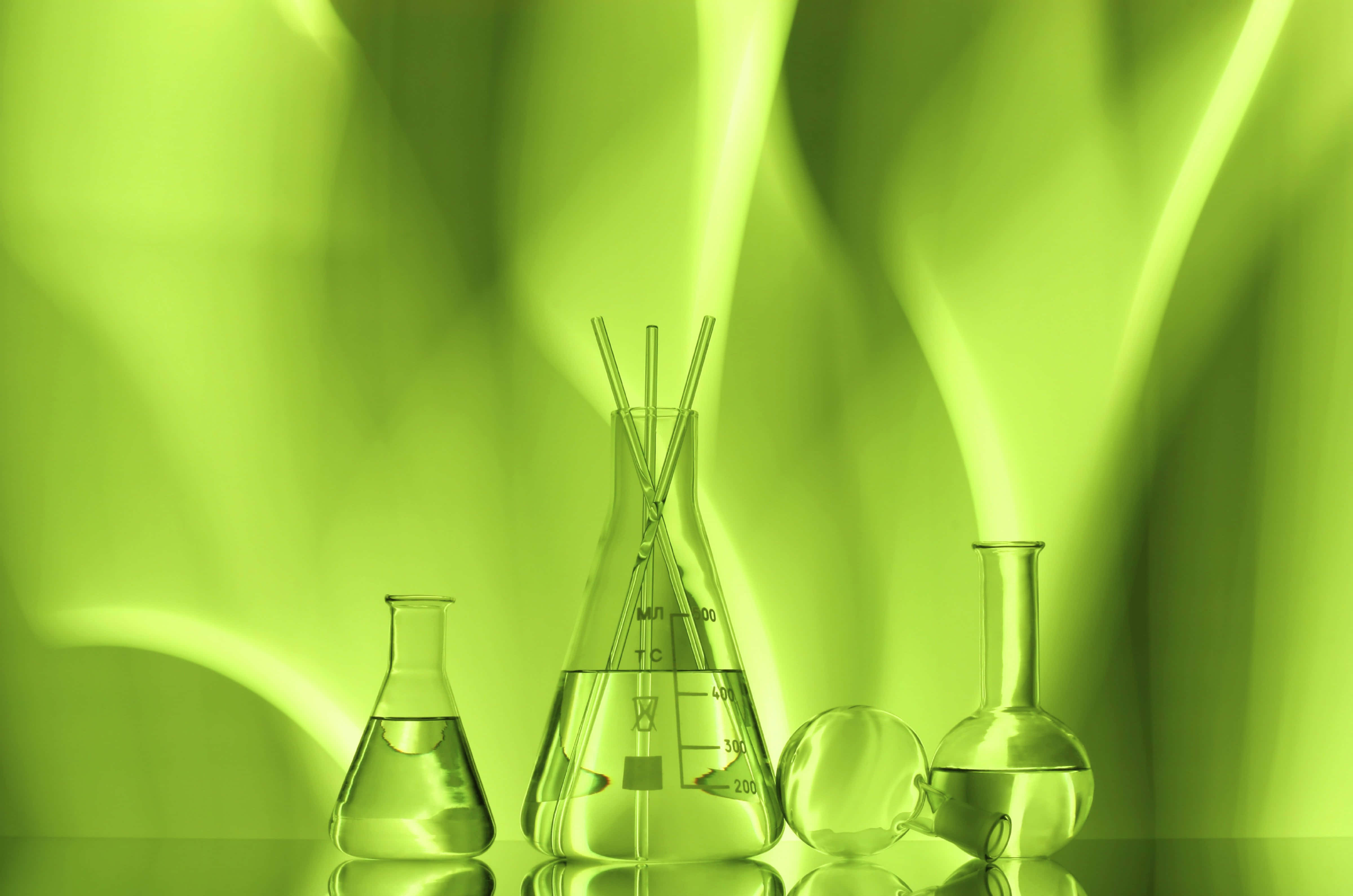 Chemistry 桌布 壁紙 — 裝滿發光綠色液體的玻璃實驗室燒瓶和燒杯放置在反光表面上，背景是充滿活力的抽象綠色。