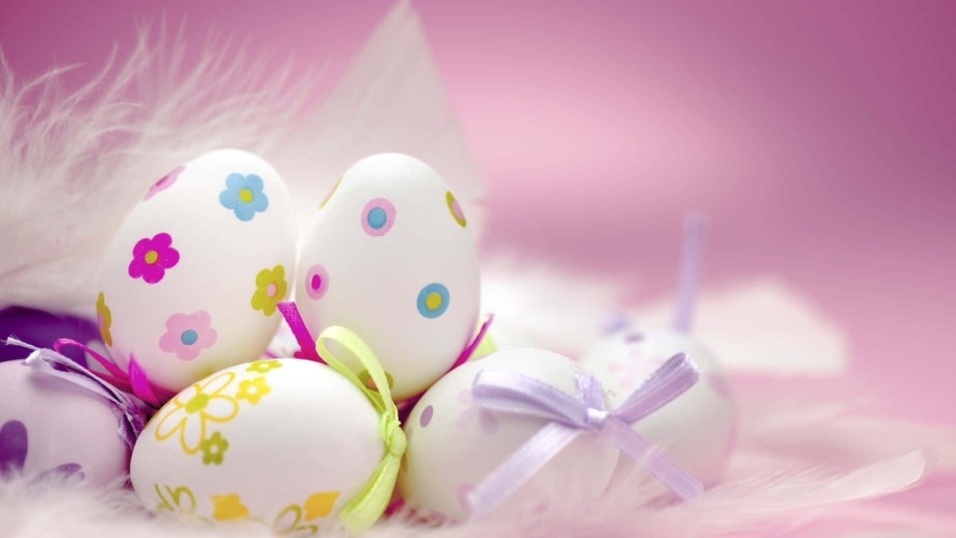 Cute Easter 桌布 壁紙 — 裝飾復活節彩蛋帶有色彩繽紛的花卉圖案和絲帶，放置在柔軟的白色羽毛上，背景是夢幻的粉紅色。