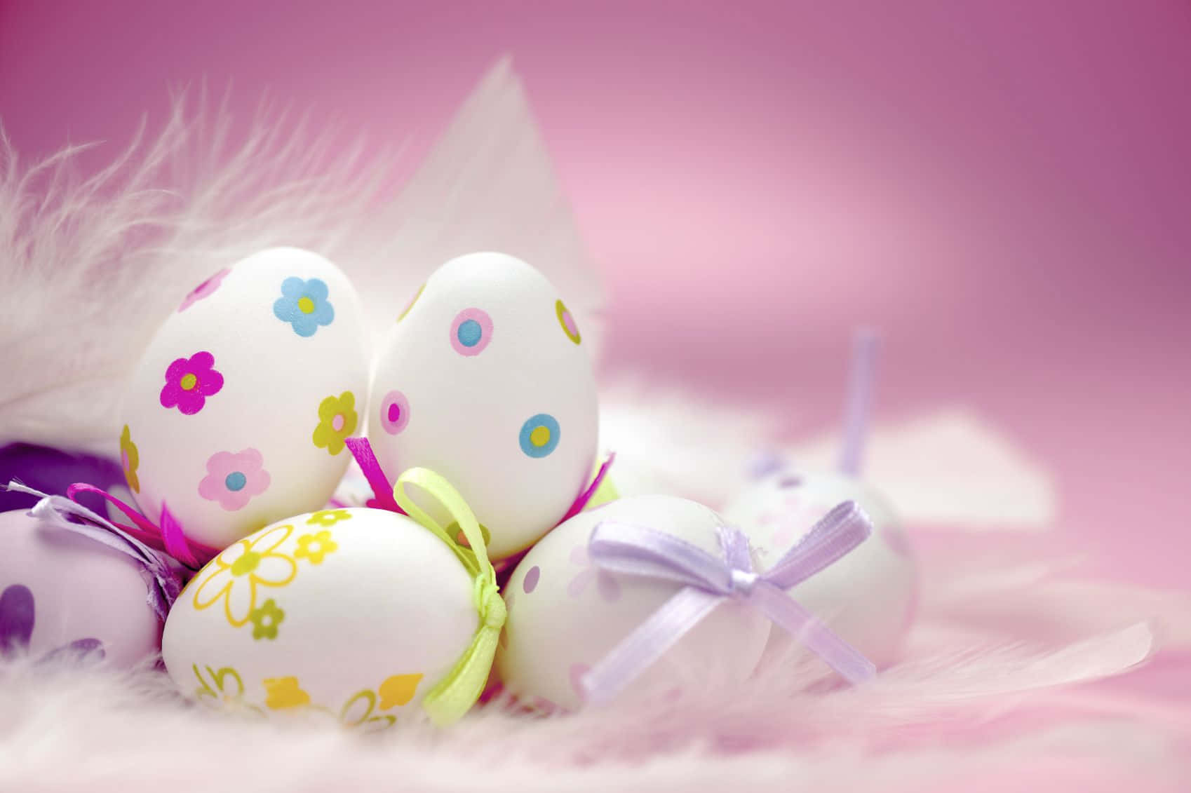 Pastel Easter 桌布 壁紙 — 裝飾有花卉圖案和絲帶的復活節彩蛋，放置在柔軟的粉紅色羽毛上，背景是夢幻的粉彩。