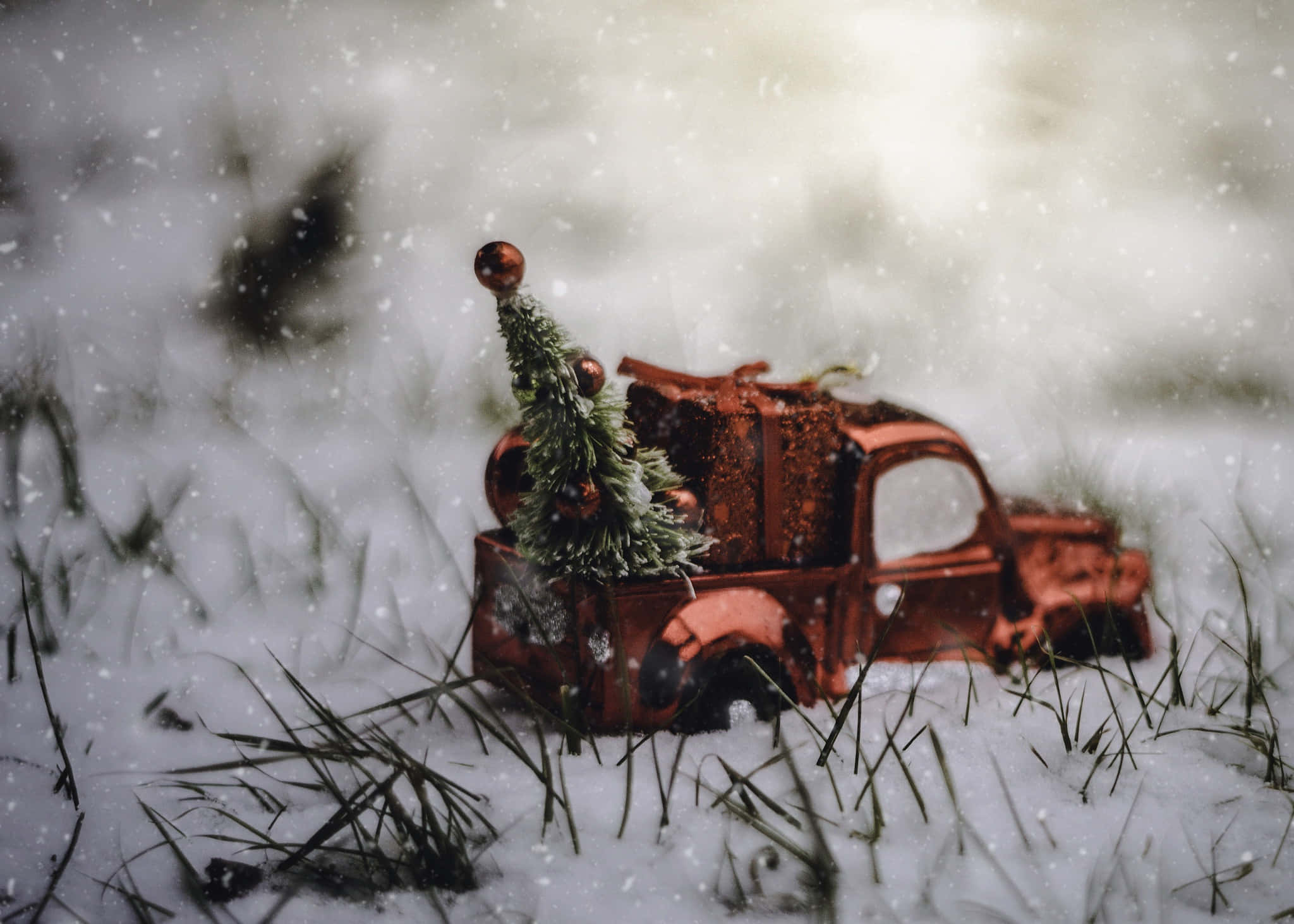 裝飾聖誕節的老式皮卡車 壁紙 — 一架生鏽的紅色玩具卡車在雪地裡載著迷你聖誕樹和禮物，雪花飄落。