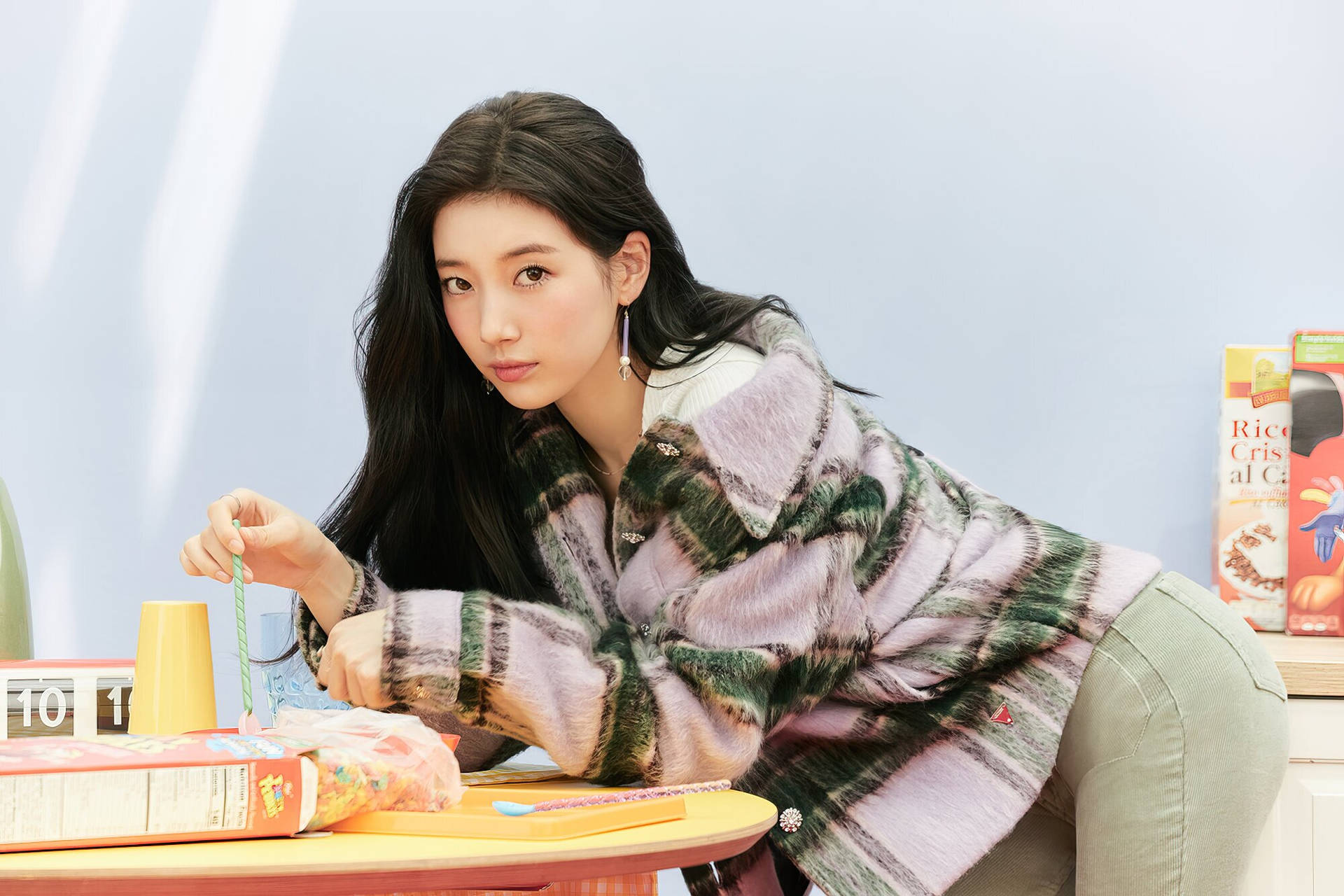 身穿圖案外套的年輕女子俯身靠近放有穀物盒和吸管的桌子。