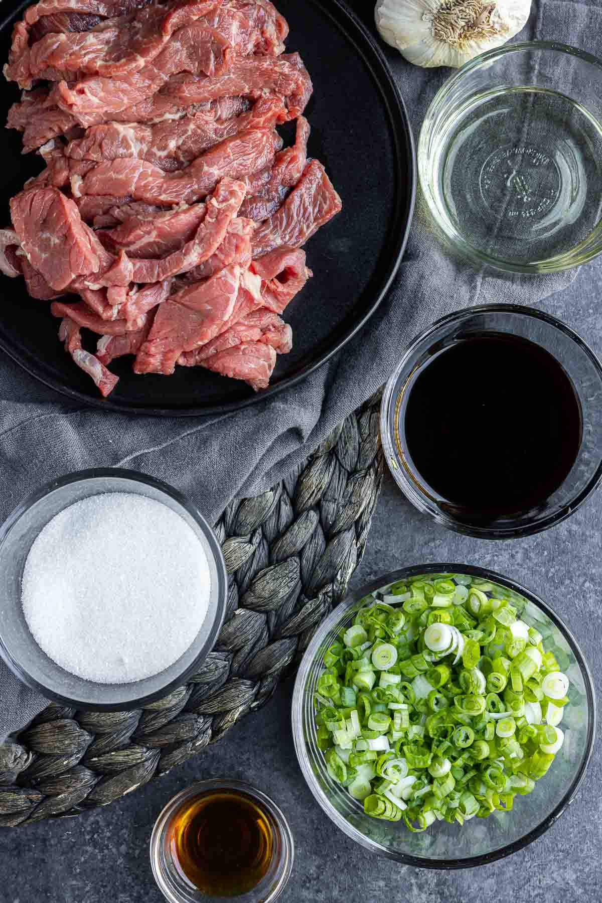 製作韓式醬油牛肉的鮮食材 壁紙 — 俯視圖：生牛肉條、糖、醬油、蒜頭和切碎嘅青蔥排列喺深色紋理表面上。