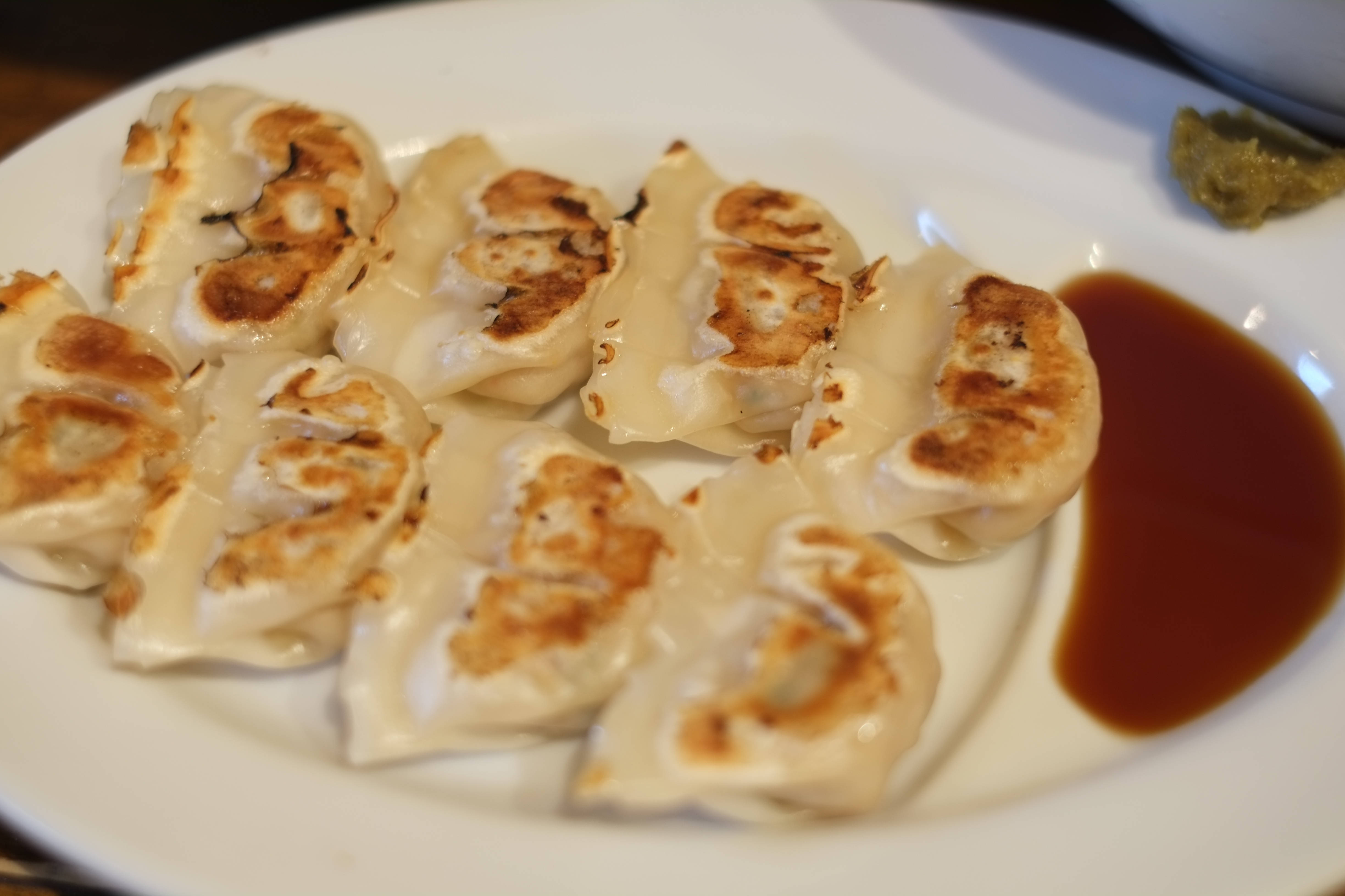 褐醬波蘭餃子 壁紙 — 金黃色的煎餃子在白色碟子上閃閃發光，旁邊是一灘深色蘸醬。