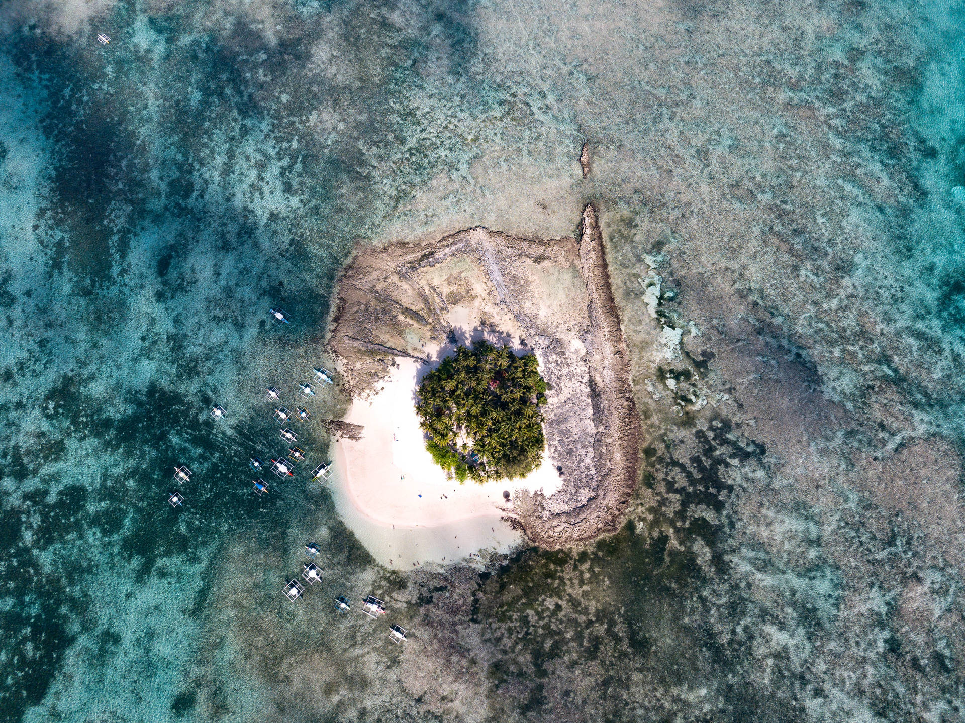 一個小型熱帶島嶼的鳥瞰圖，擁有白色沙灘和停泊在碧綠海水中的船隻。