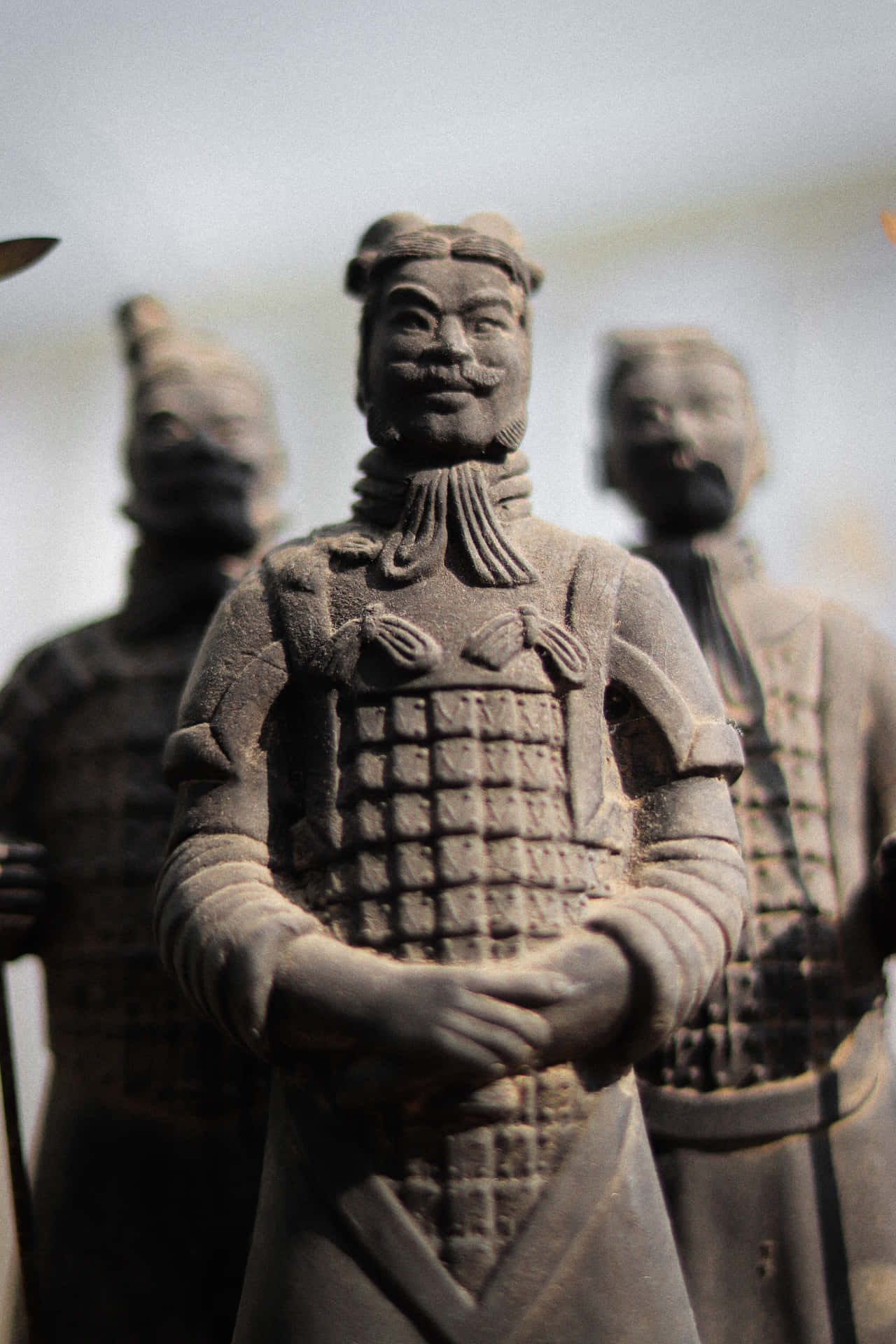西安兵馬俑的壯麗景象 壁紙 — 詳細兵馬俑雕像的特寫，具有複雜的盔甲和寧靜的表情，周圍是模糊的同伴士兵。