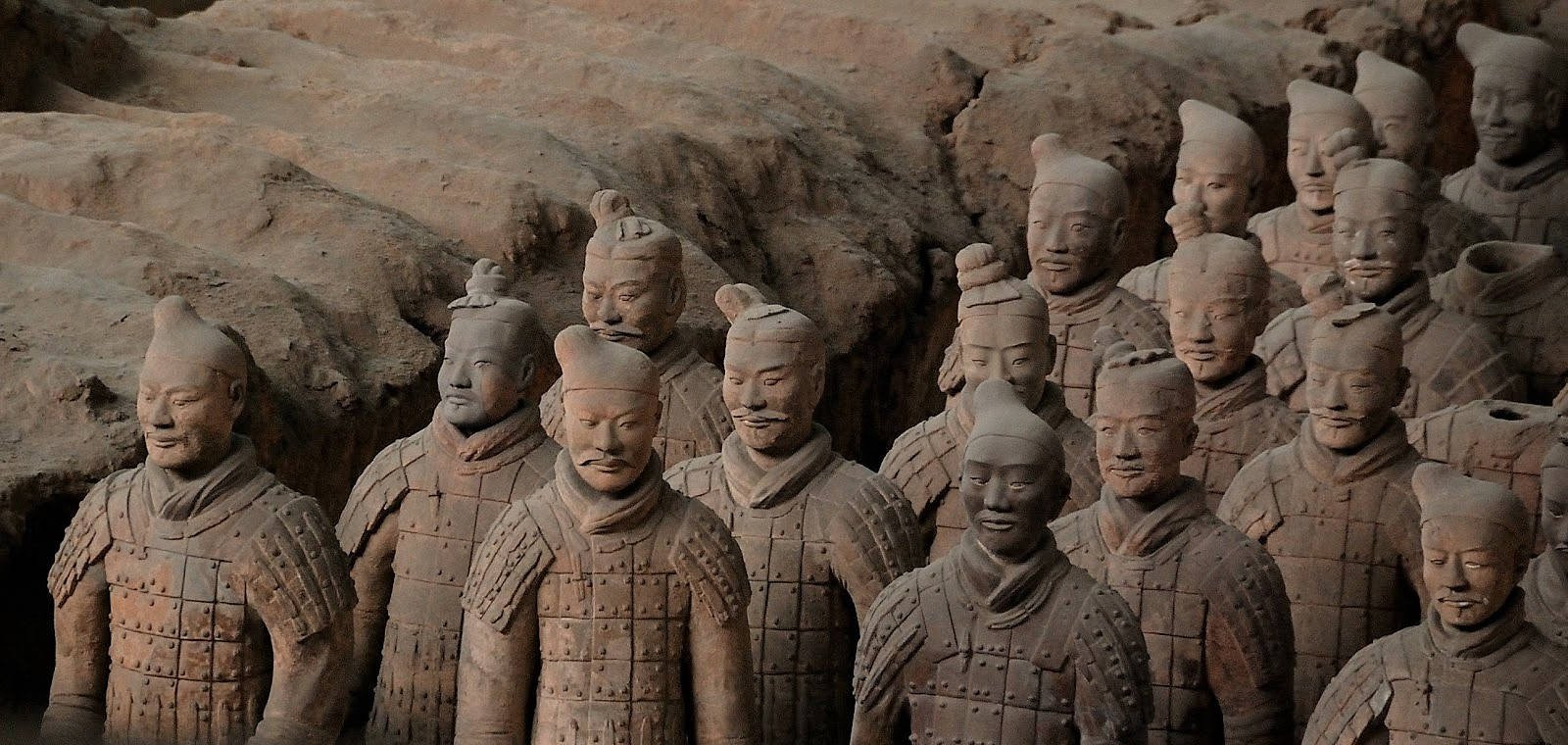 西安古代人形雕像 壁紙 — 一排排古老的兵馬俑莊嚴地矗立在發掘坑中，帶有泥土色調和風化細節。