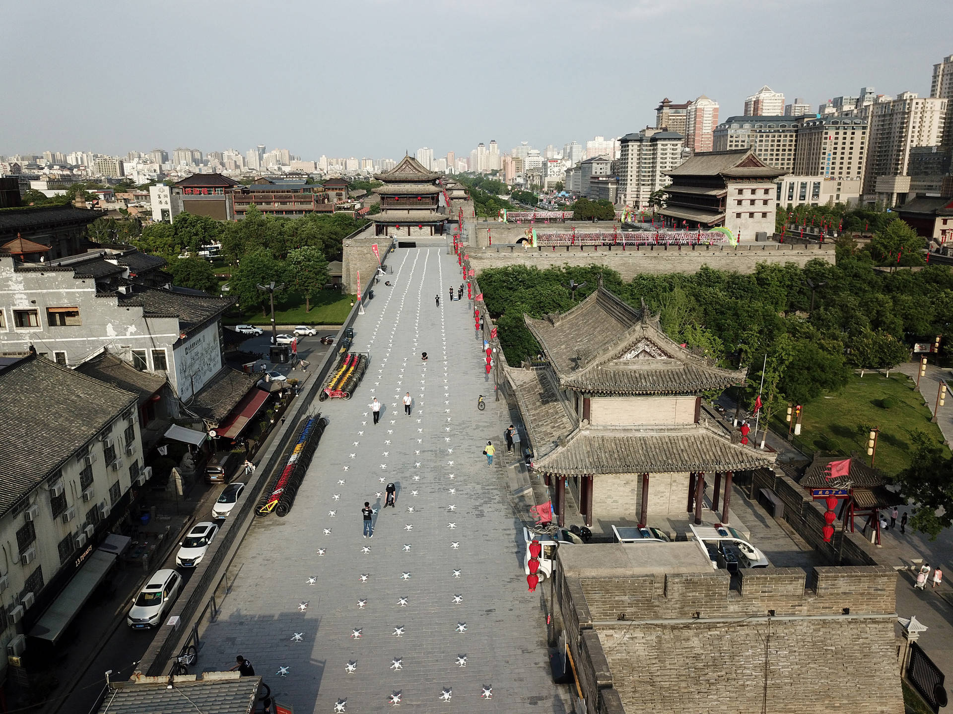 西安古城牆壯麗景觀 壁紙 — 古代中國城牆的鳥瞰圖，遊客沿著鋪砌的小路行走，兩旁是傳統建築和現代建築，天空朦朧。
