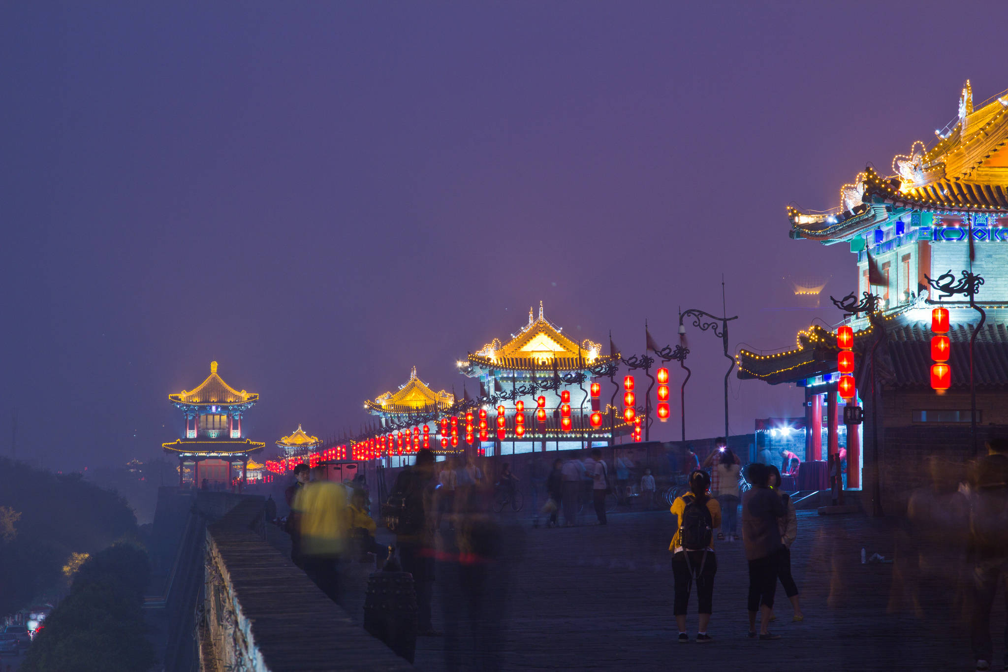 西安城牆霧夜 壁紙 — 歷史中國城牆的夜景，金色燈籠和閃爍的寶塔屋頂照亮，模糊的行人沿著小路行走。
