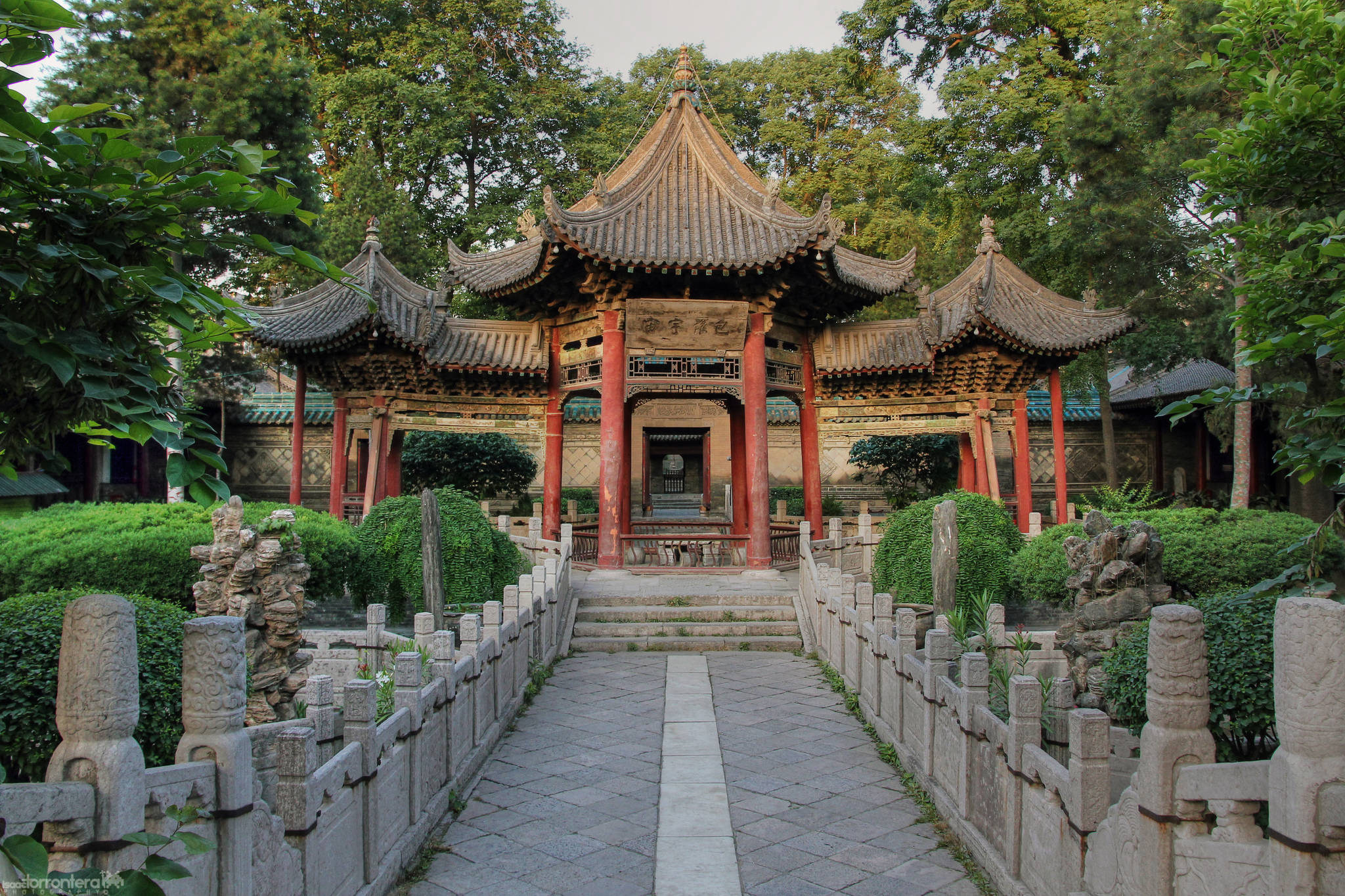 西安大清真寺 壁紙 — 一座傳統中式亭閣，紅柱曲瓦頂，矗立於石徑盡頭，兩旁是修剪整齊的樹籬和古樹。