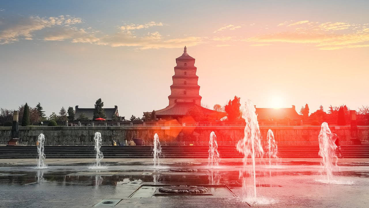 西安寶塔紅霞夕照 壁紙 — 一座宏偉的古塔在溫暖的日落天空下呈現剪影，前景中噴泉噴灑著水花。