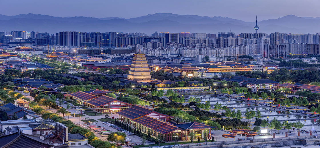 西安空中鳥瞰 壁紙 — 暮色中的城市景觀，融合了古老寶塔和傳統屋頂與現代摩天大樓，背景是霧濛濛的山脈。