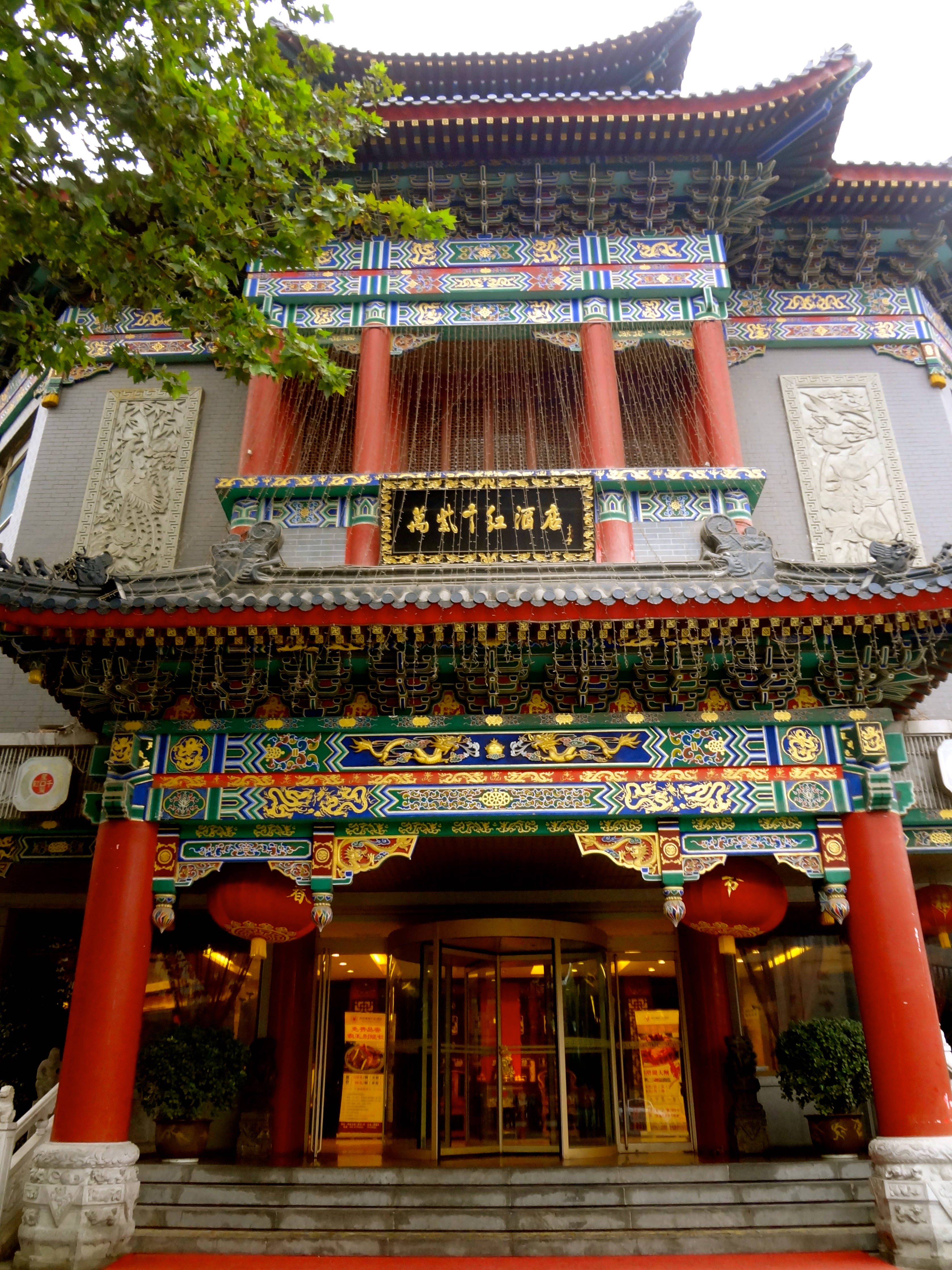 西安精緻古建築 壁紙 — 一座宏偉的傳統中式建築，擁有紅色柱子、華麗屋頂和懸掛的燈籠，在明亮的天空下。