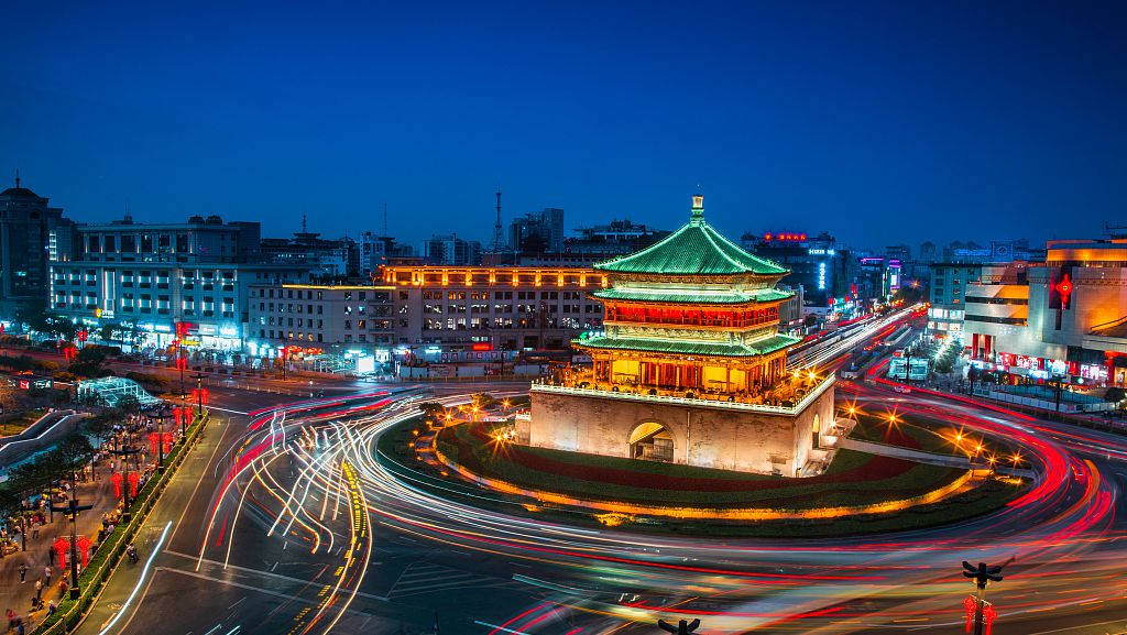 西安鐘樓 壁紙 — 一座歷史悠久的中國塔在黃昏時分溫暖地發光，汽車燈光在繁忙的城市迴旋處圍繞它旋轉。