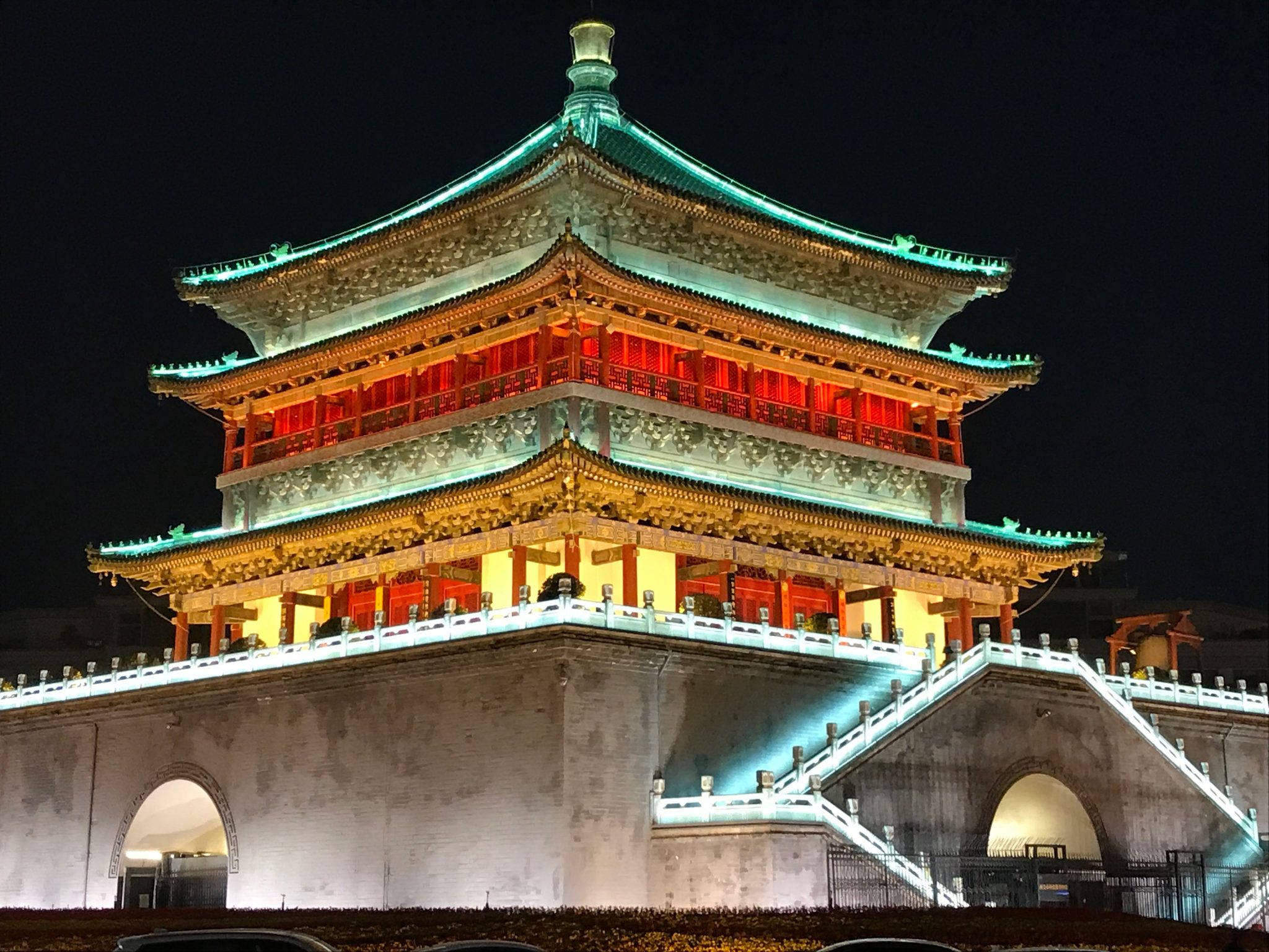 西安鐘樓夜景 壁紙 — 一座宏偉的傳統中式塔樓在夜間被紅色和青綠色的燈光照亮，襯托著黑暗的天空。