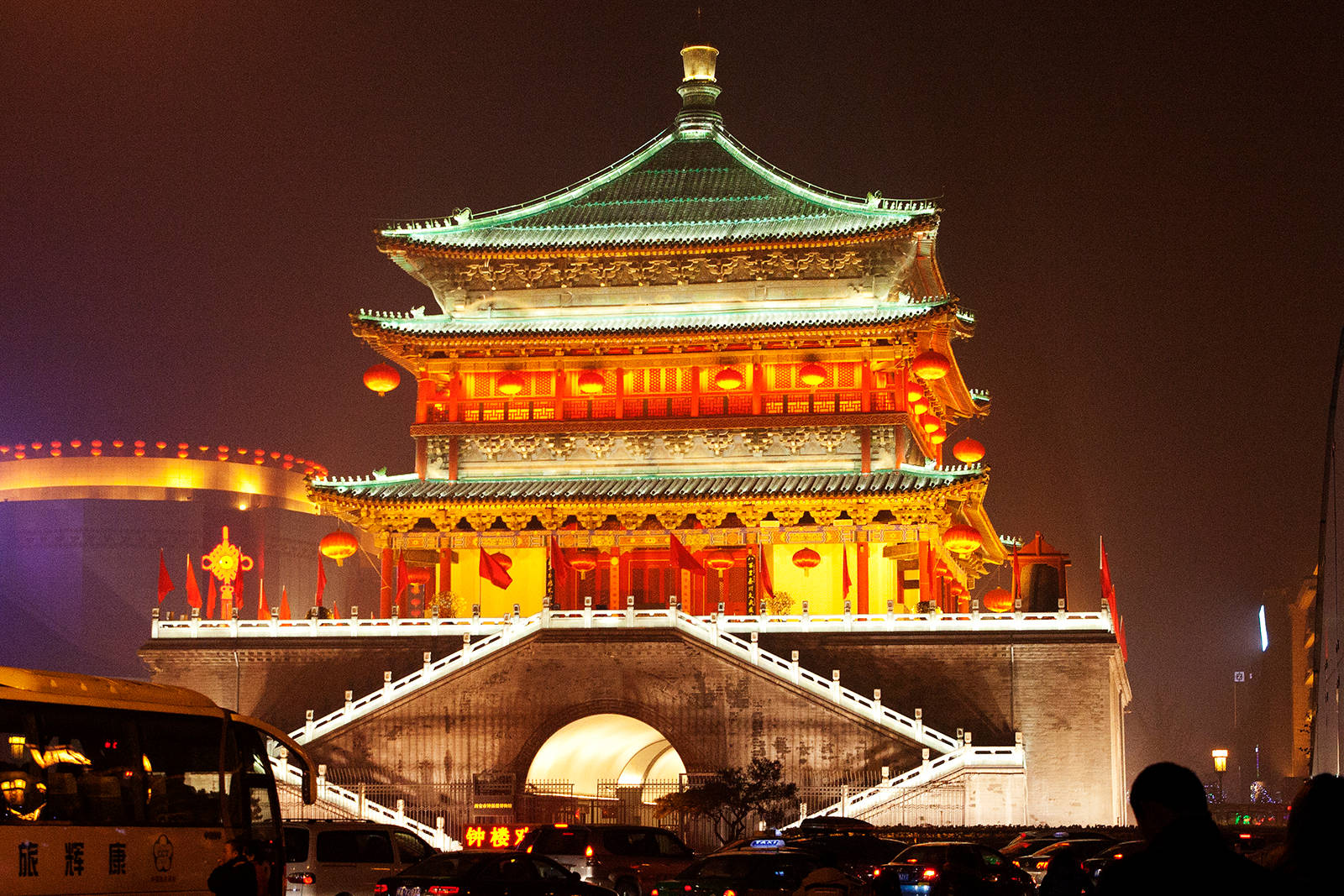 西安鐘樓夜景輝煌 壁紙 — 一座宏偉的傳統中式塔樓，在深色夜空下以溫暖的橙色和綠色燈光照亮，下方車水馬龍。