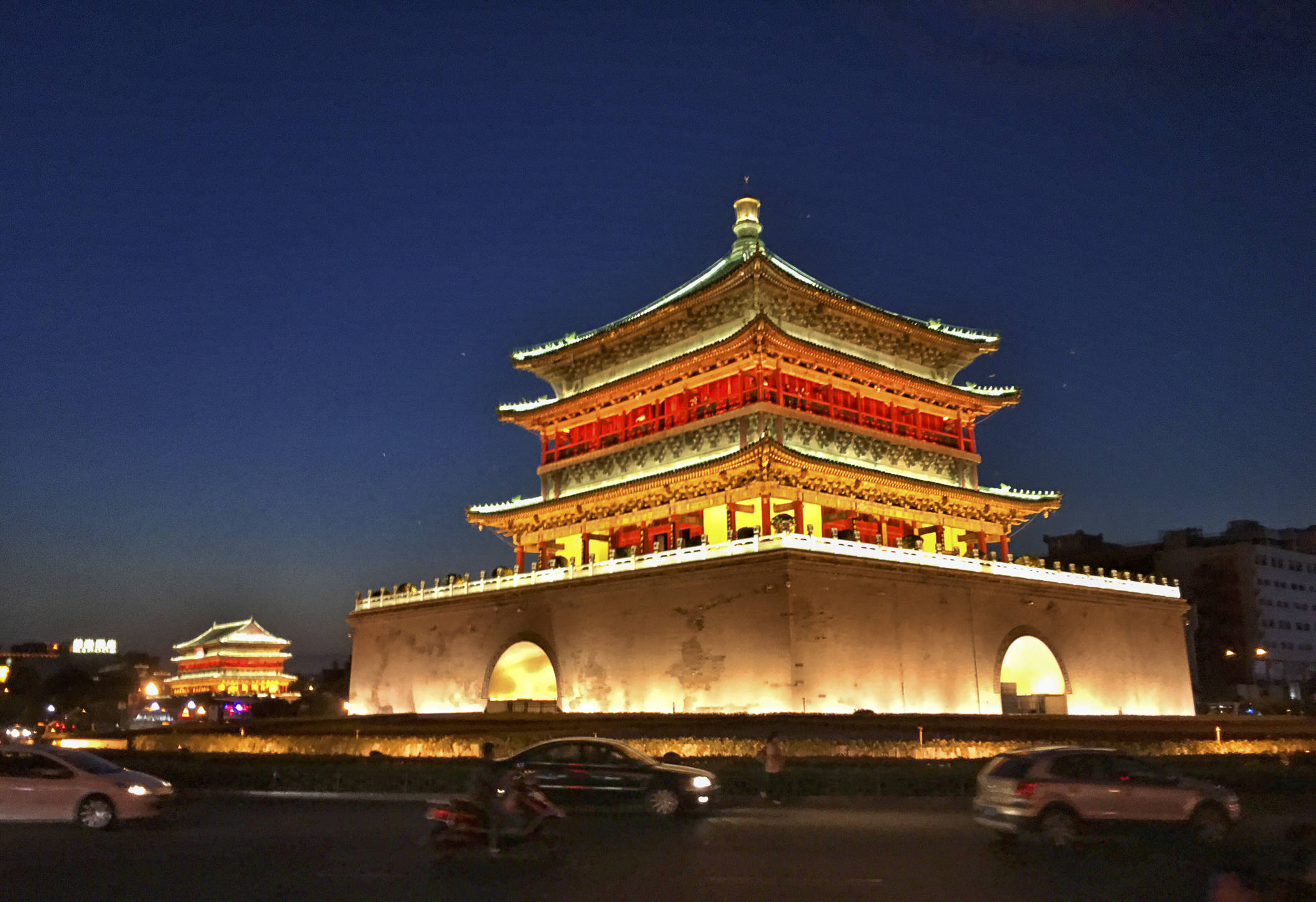 西安鐘樓黃昏盛景 壁紙 — 一座宏偉的傳統中式塔樓在深藍色夜空下溫暖地發光，汽車駛過。