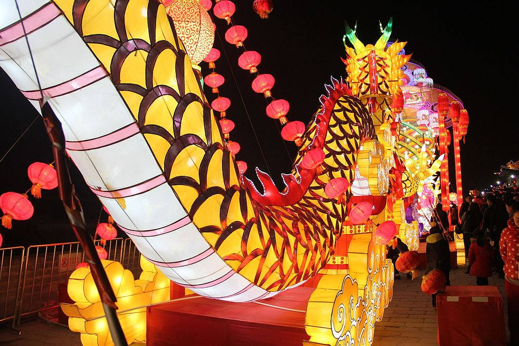 西安龍燈節 壁紙 — 一個巨大發光的黃色龍燈籠，帶有紅色點綴和懸掛的粉紅色燈籠，照亮了夜間節日的街道。