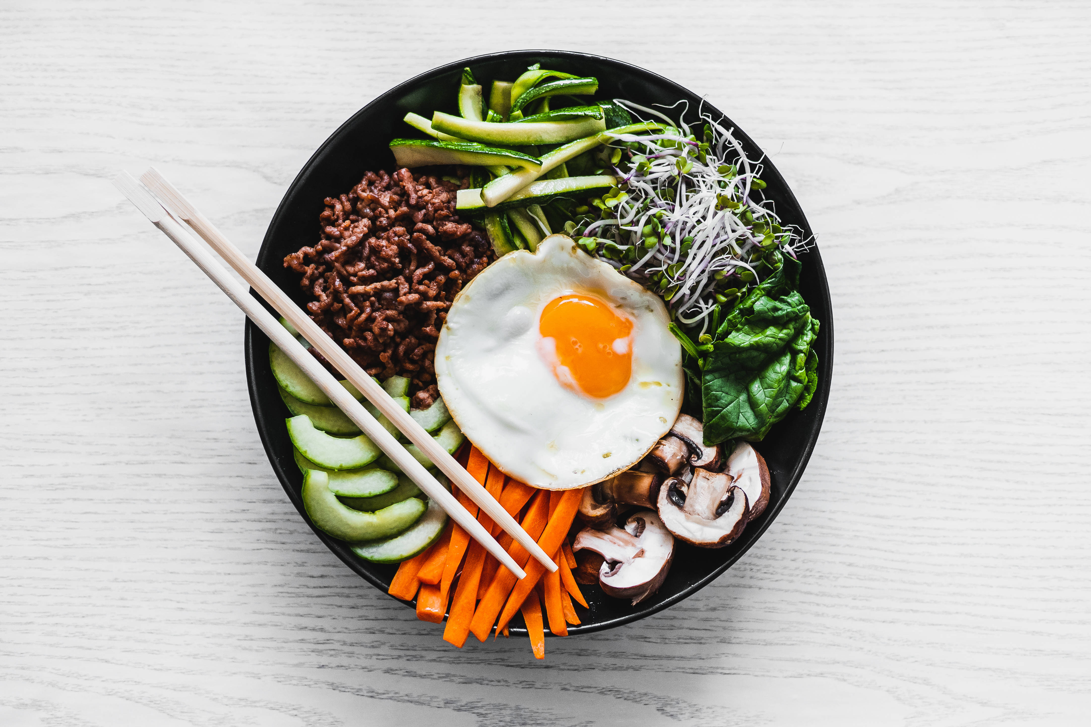 西式風格韓式拌飯 壁紙 — 一個充滿活力的韓國拌飯碗，上面放著太陽蛋和色彩繽紛的蔬菜，置於白色木桌上。