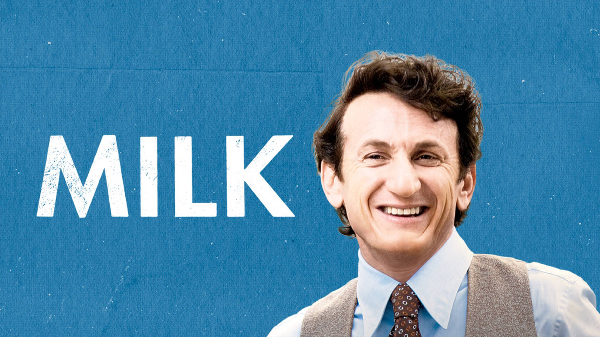 一個穿著背心同領帶嘅男人，喺藍色牆上MILK字樣旁邊微笑。