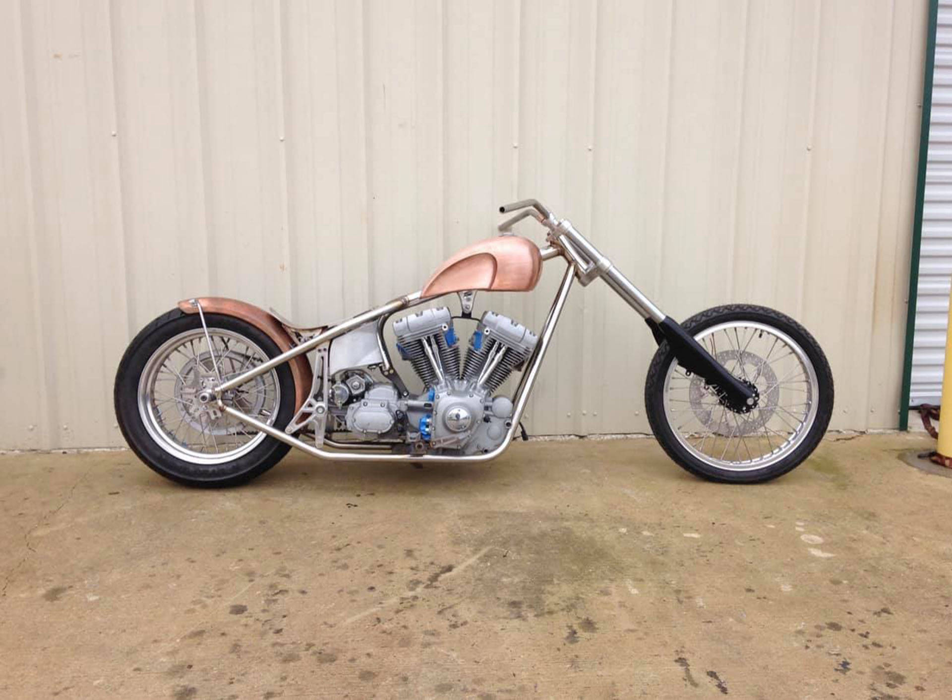 西海岸車廠Bobber摩托車 壁紙 — 一架定制嘅chopper電單車，帶有銅色點綴同鉻合金細節，停泊喺米色金屬牆邊。
