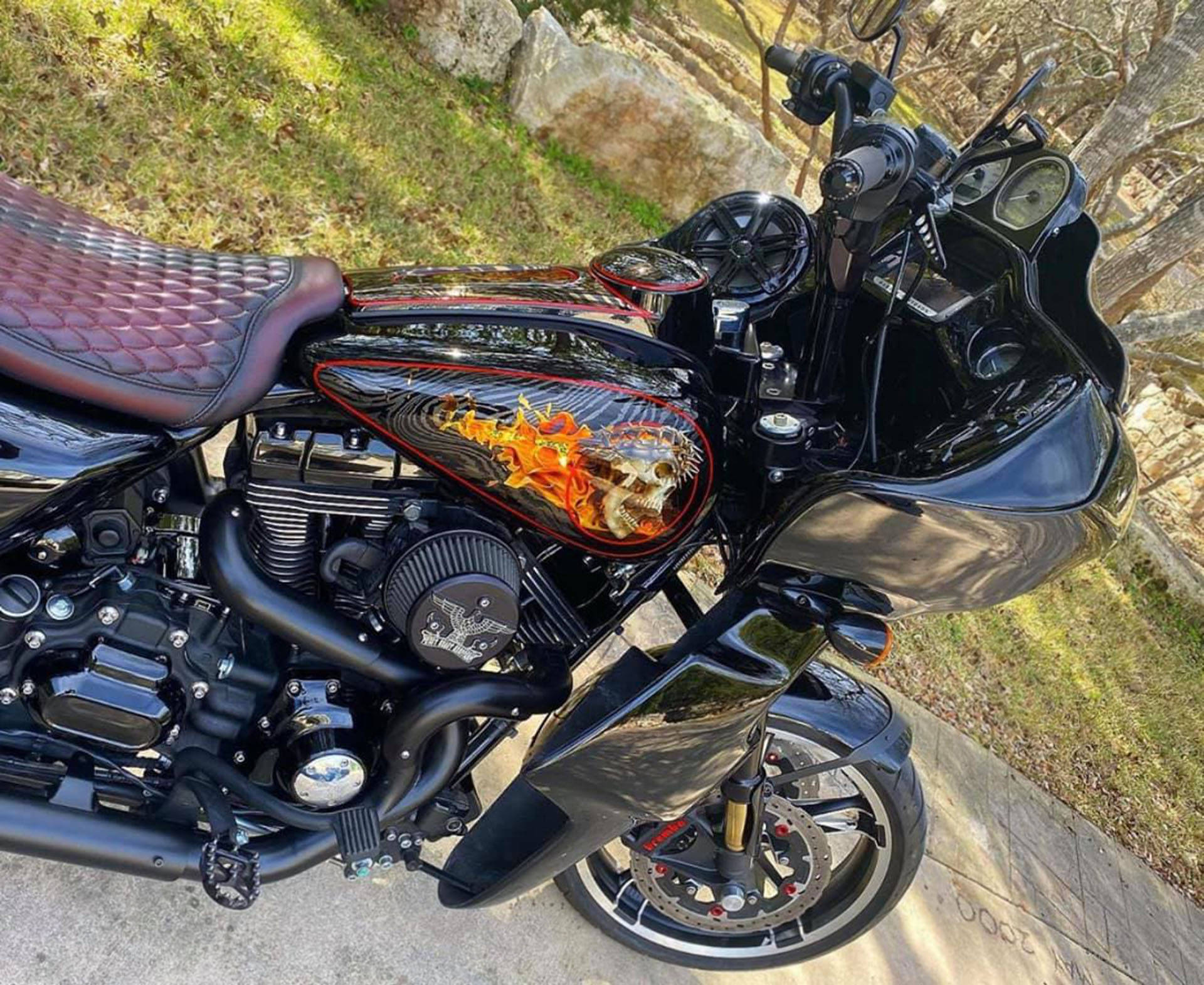 西海岸車廠自訂Road Glide 壁紙 — 一架亮黑色訂製電單車，油箱上有火焰骷髏圖案，停泊在草地旁邊的混凝土小徑上。