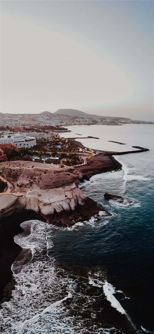 黃昏時分的沿海小鎮，海浪拍打火山懸崖和遠處的山脈。