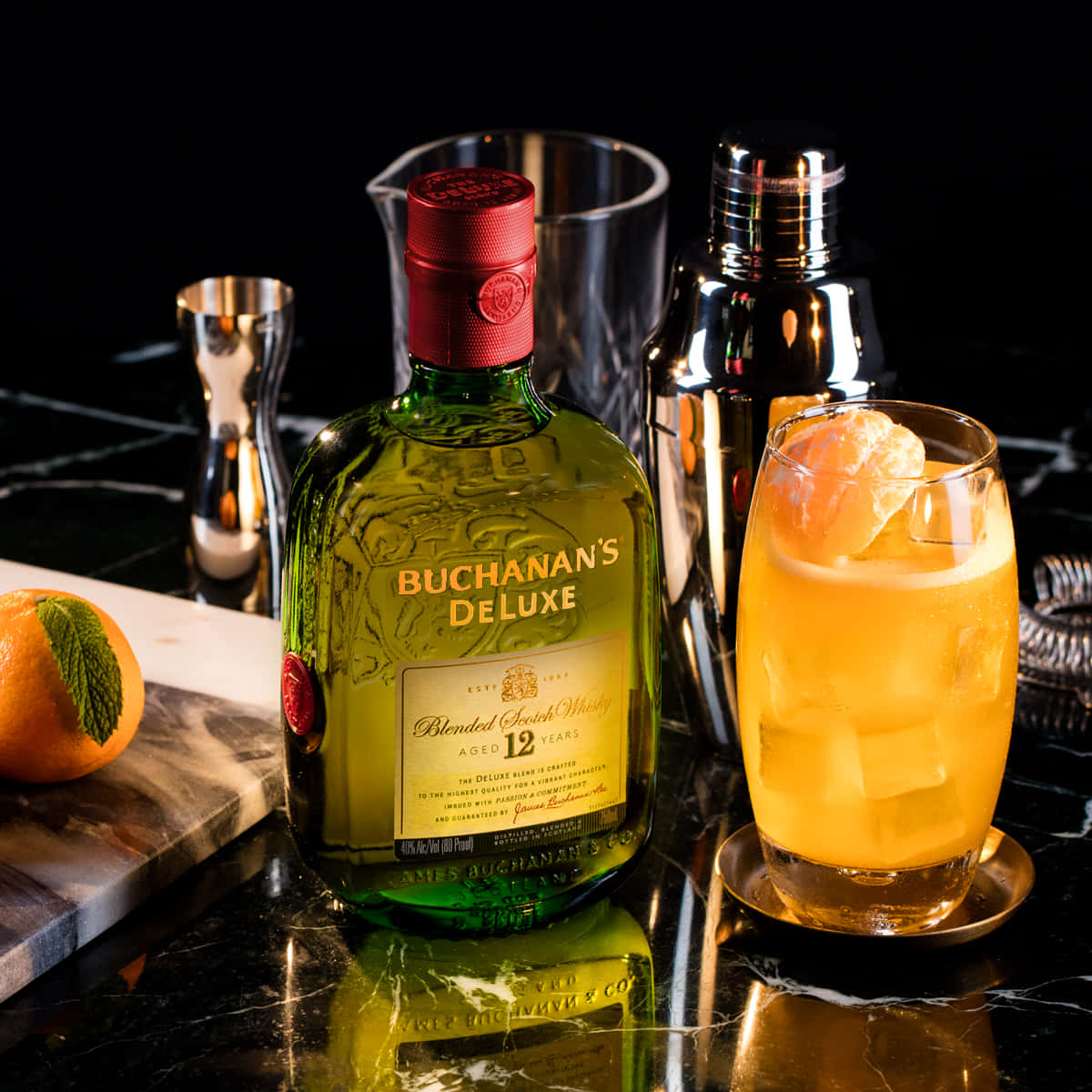 黑色雲石吧枱上嘅 Buchanan's Deluxe 威士忌酒瓶同雞尾酒，配上橙裝飾。