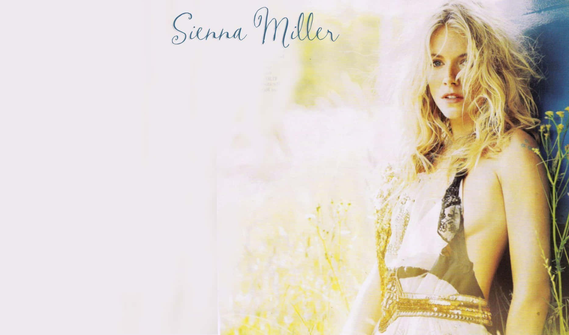 Sienna Miller 穿著帶有金色飾邊的白色連衣裙，站在陽光明媚的田野中。