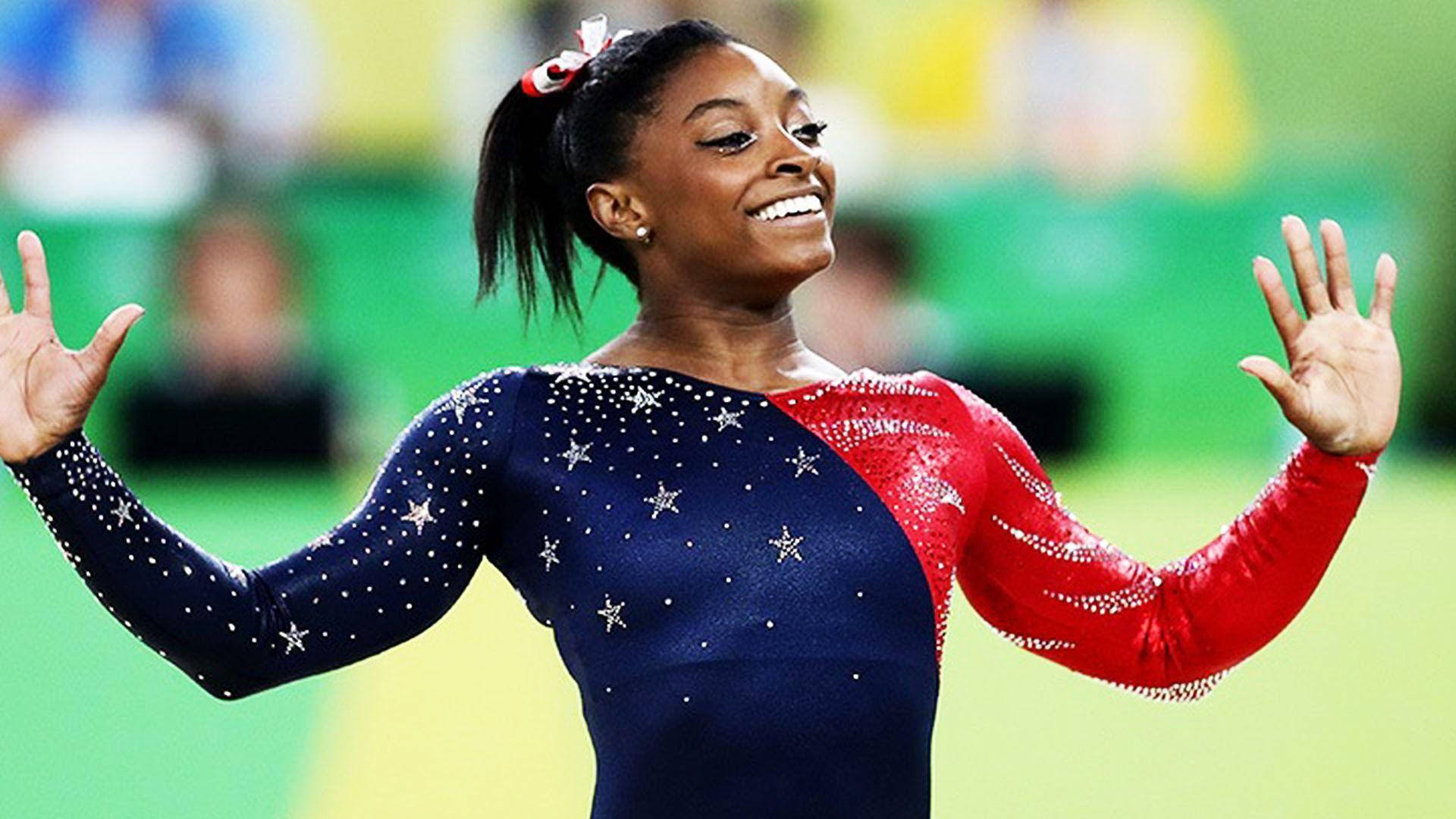 體操運動員Simone Biles身穿星條旗緊身衣，張開雙臂慶祝。